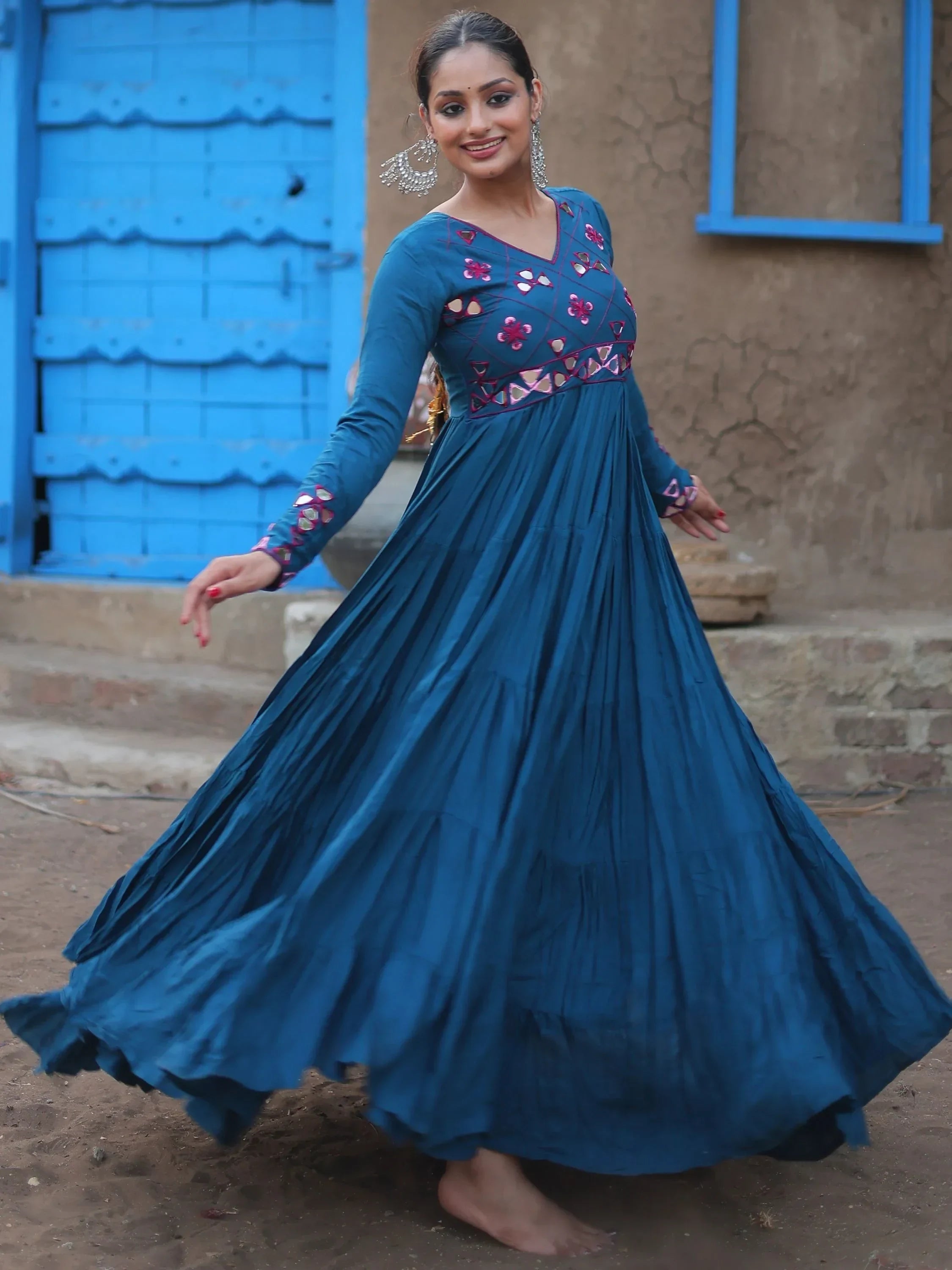 Woman in blue embroidered ethnic gown twirling outdoors, traditional Indian attire