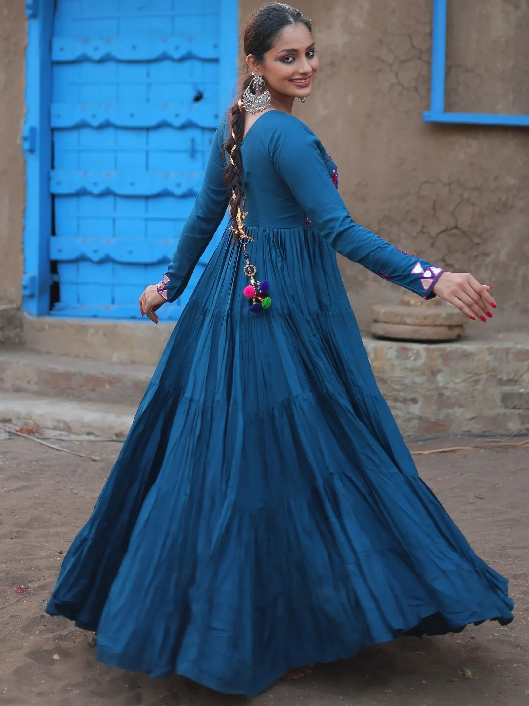 Woman in blue ethnic gown with mirror work, dancing outdoors by a rustic blue door