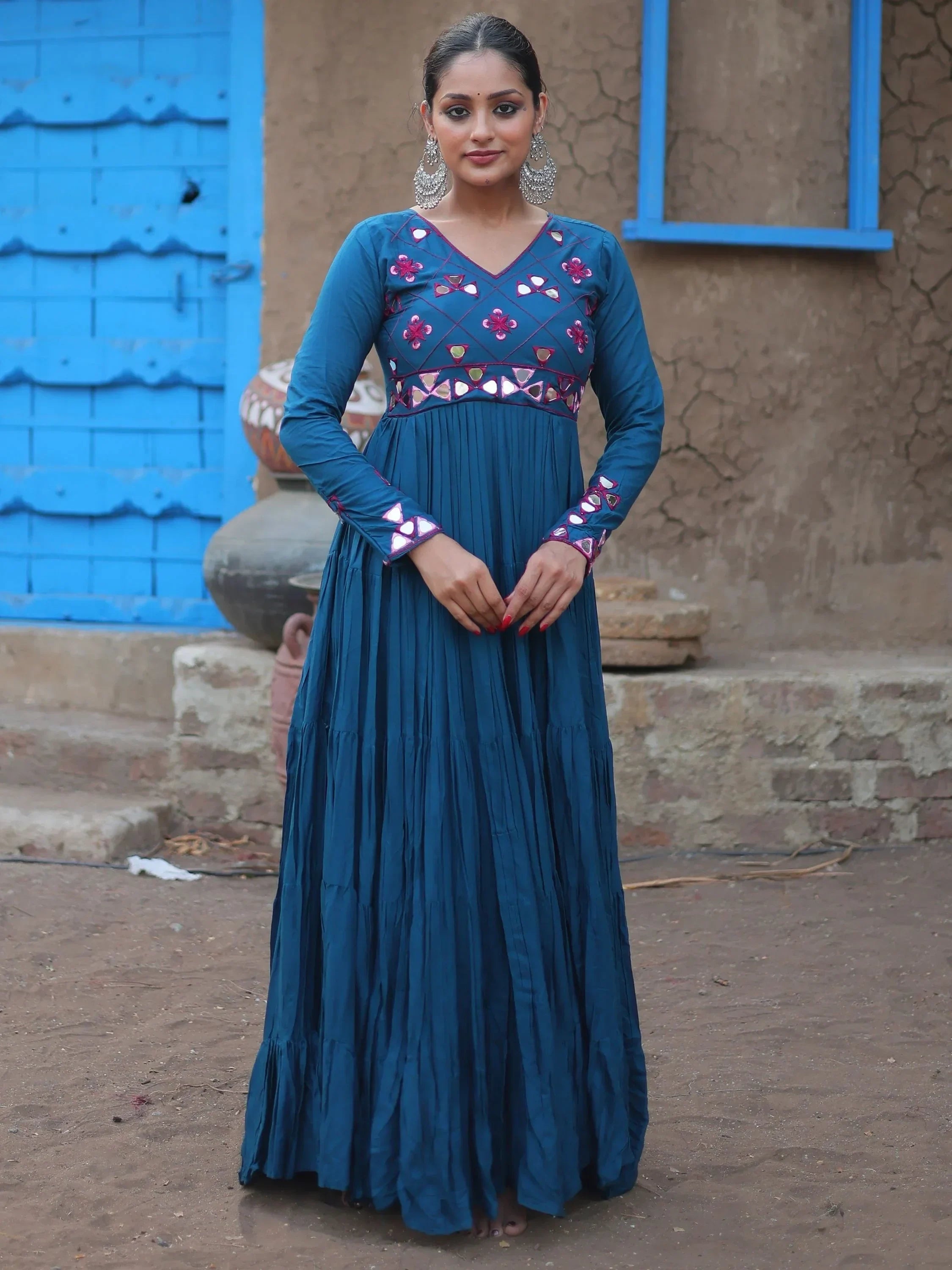 Woman wearing a blue embroidered ethnic gown with mirror detailing, standing outdoors