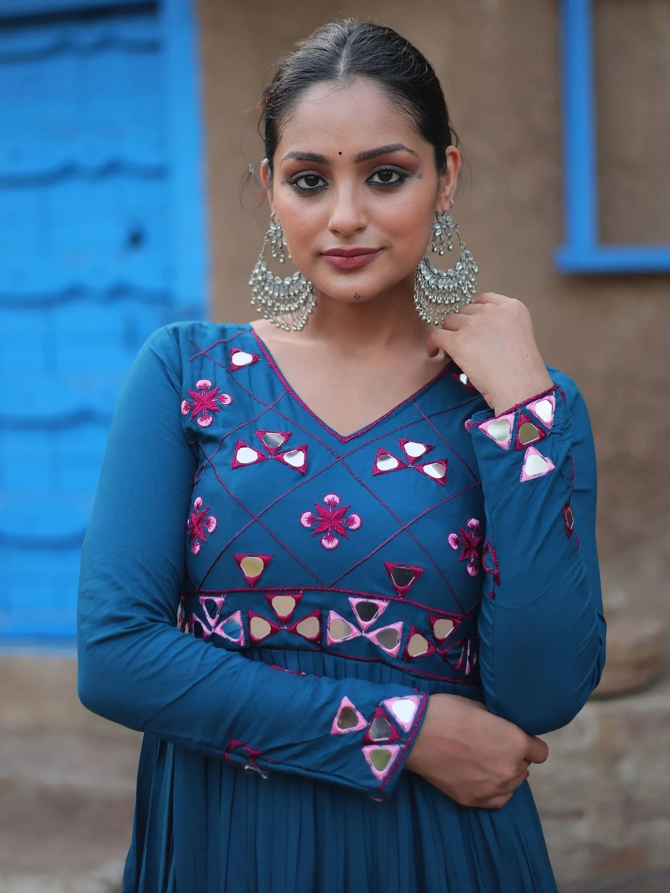 Woman wearing a blue ethnic gown with mirror work and embroidery, statement earrings, outdoor setting
