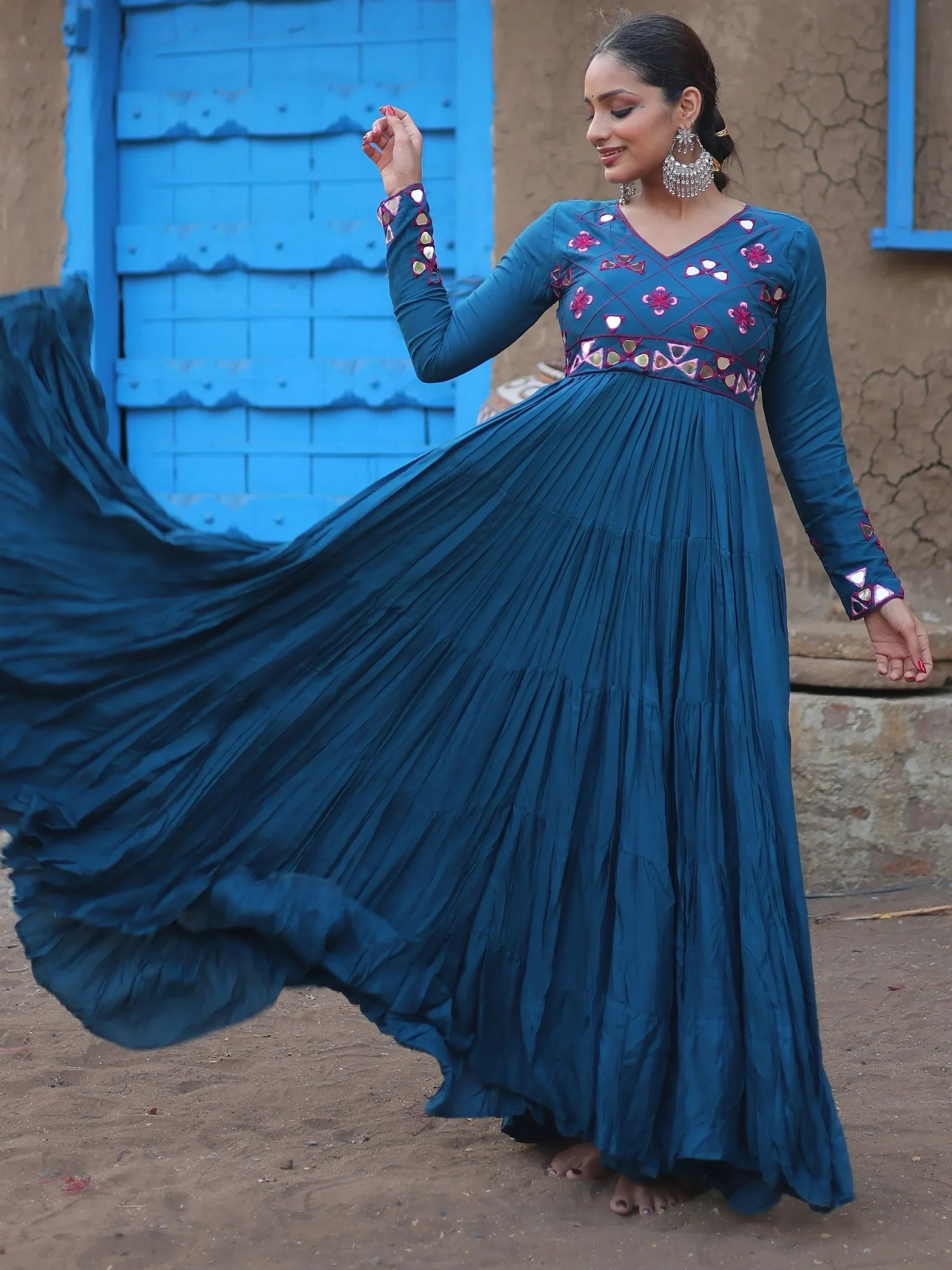 Woman in a blue embroidered ethnic gown with flared skirt, standing outdoors by a blue door