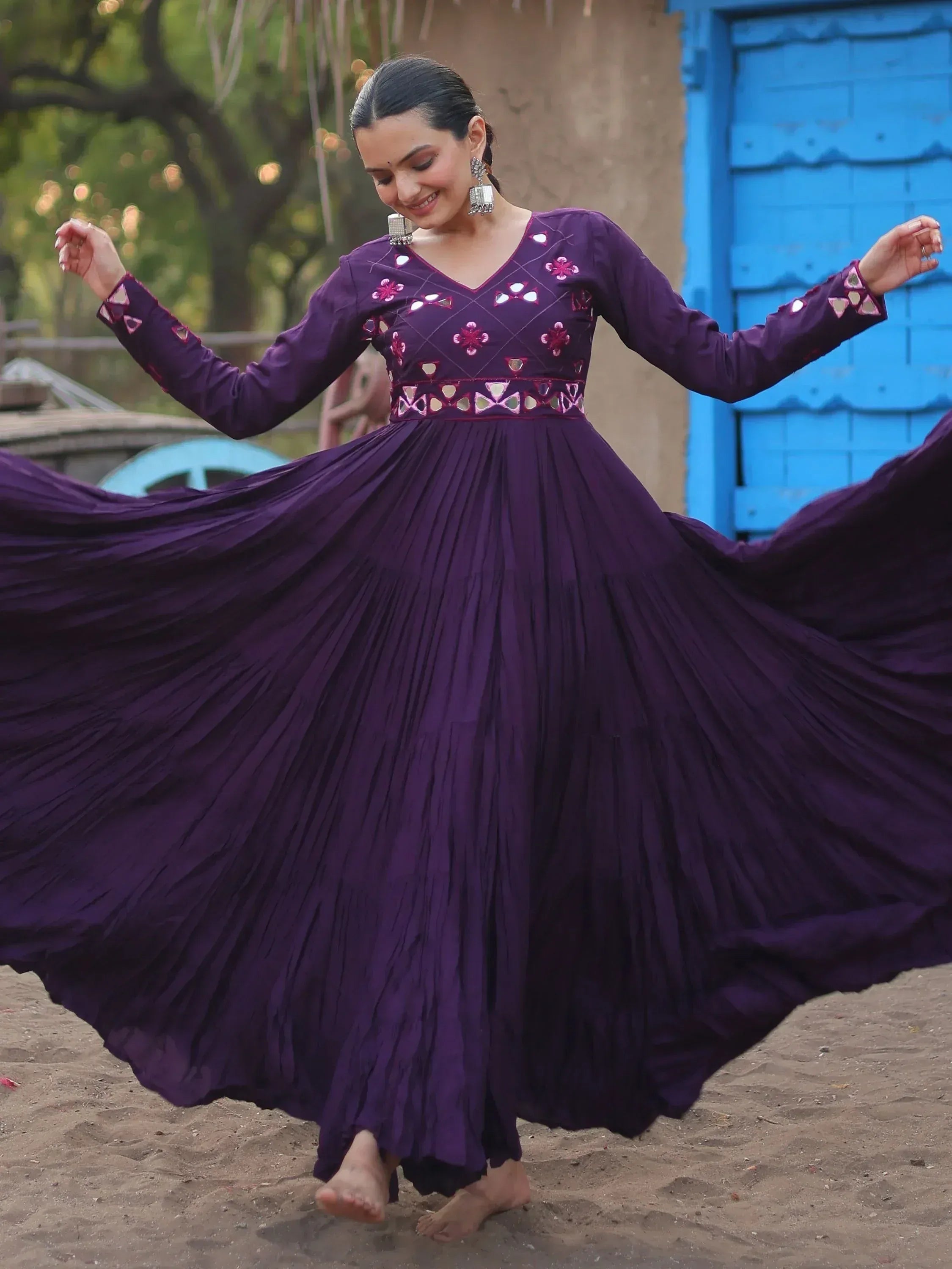Woman twirling in purple ethnic gown with mirror work, floral embroidery, and pleated skirt