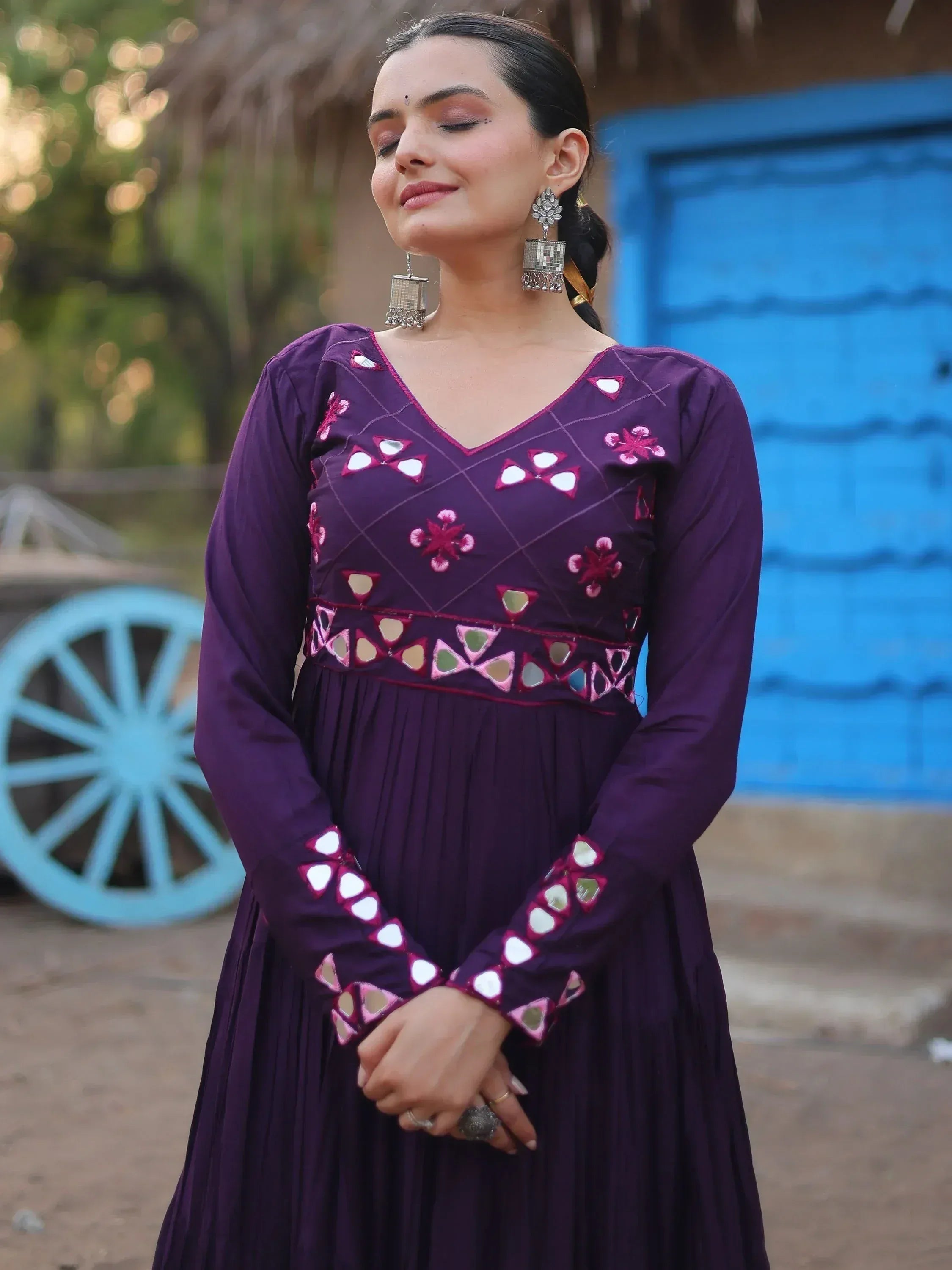 Purple ethnic gown with mirror work and floral embroidery, styled with statement earrings.