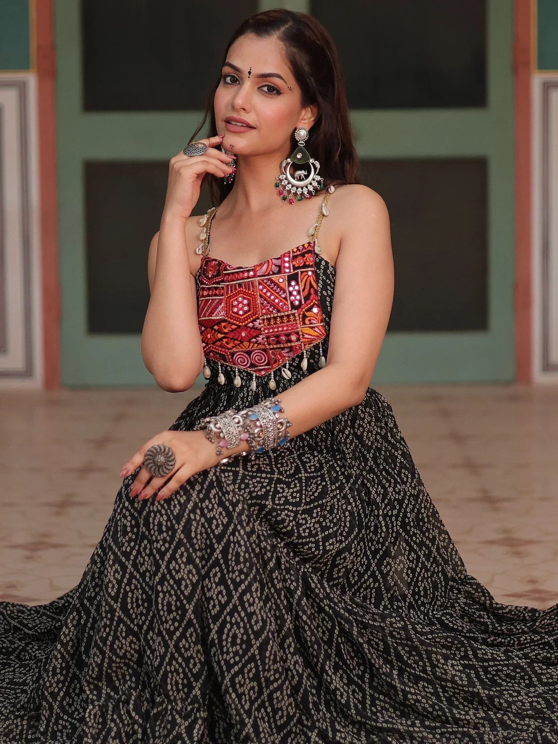 Woman in black printed ethnic gown with colorful embroidered top and traditional jewelry
