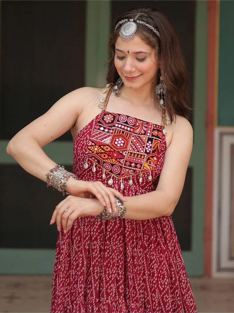 Woman in red ethnic gown with mirror work, tribal jewelry, and headpiece for festive Indian wear