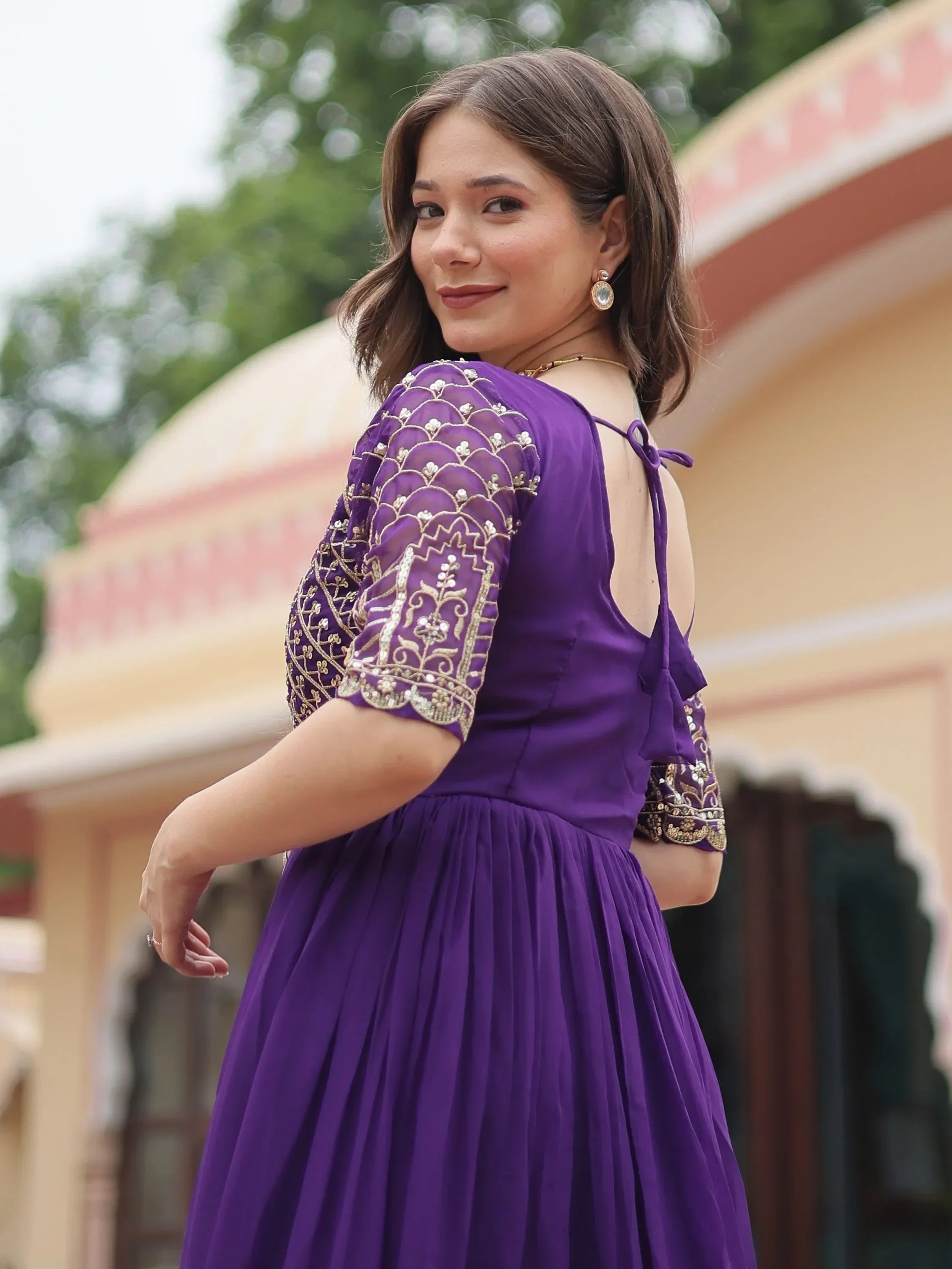 Woman in a purple embroidered ethnic gown with open back and gold detailing outdoors