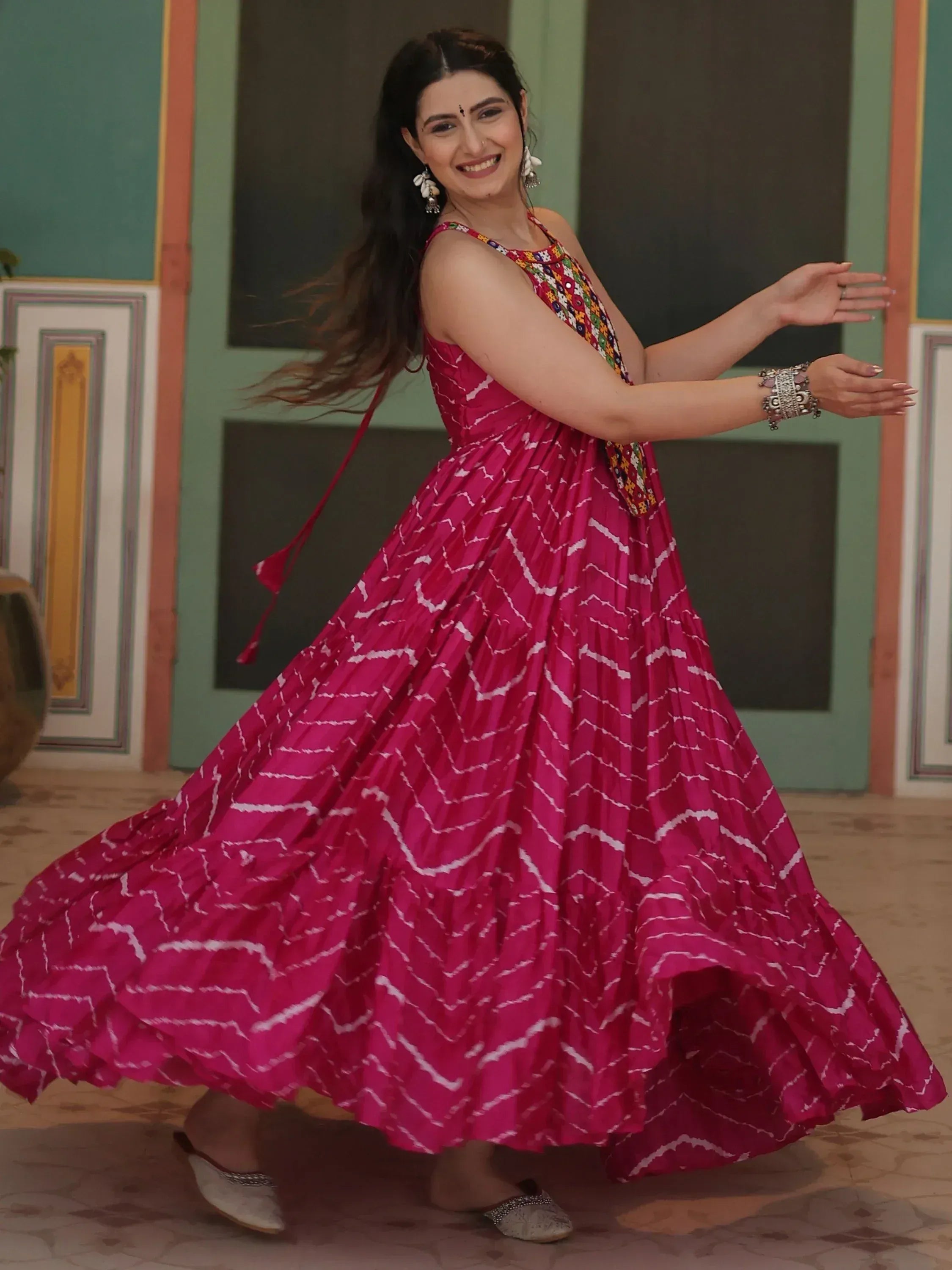 Woman twirling in vibrant pink ethnic gown with white zigzag print and embroidered bodice