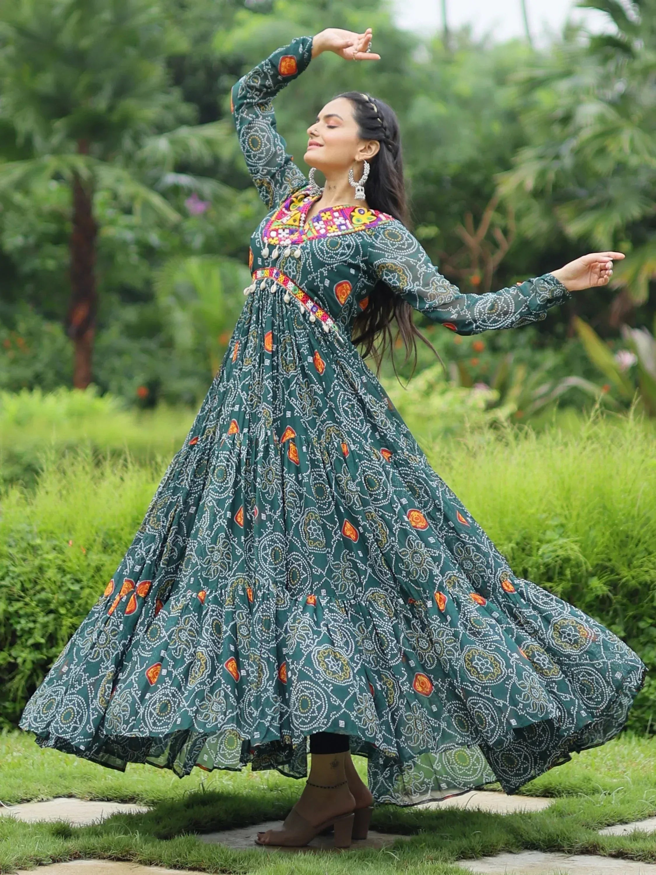Woman in green printed ethnic gown with mirror work, dancing in garden