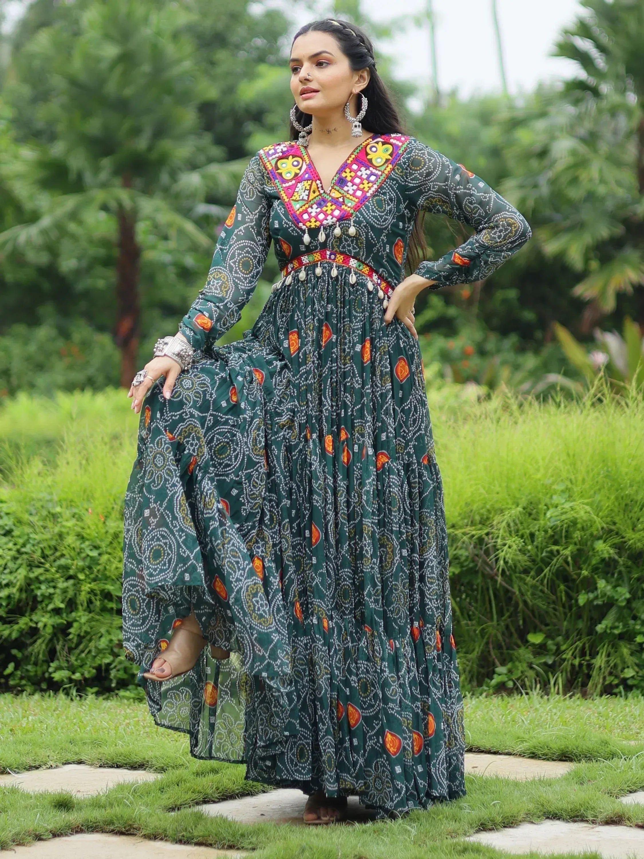 Woman in green printed ethnic gown with colorful embroidery, standing in garden
