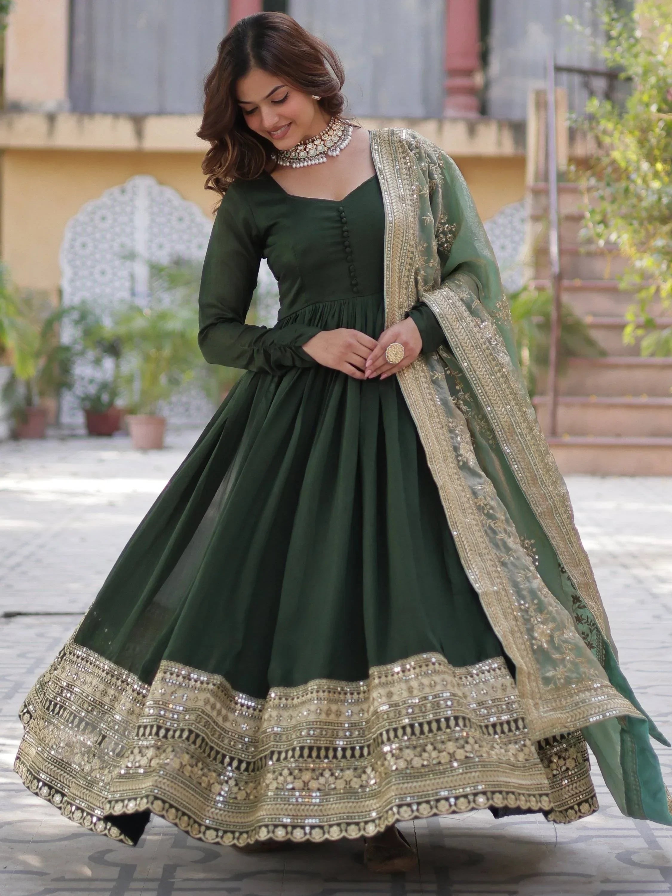Woman in a dark green ethnic gown with gold embroidered dupatta and mirror work border