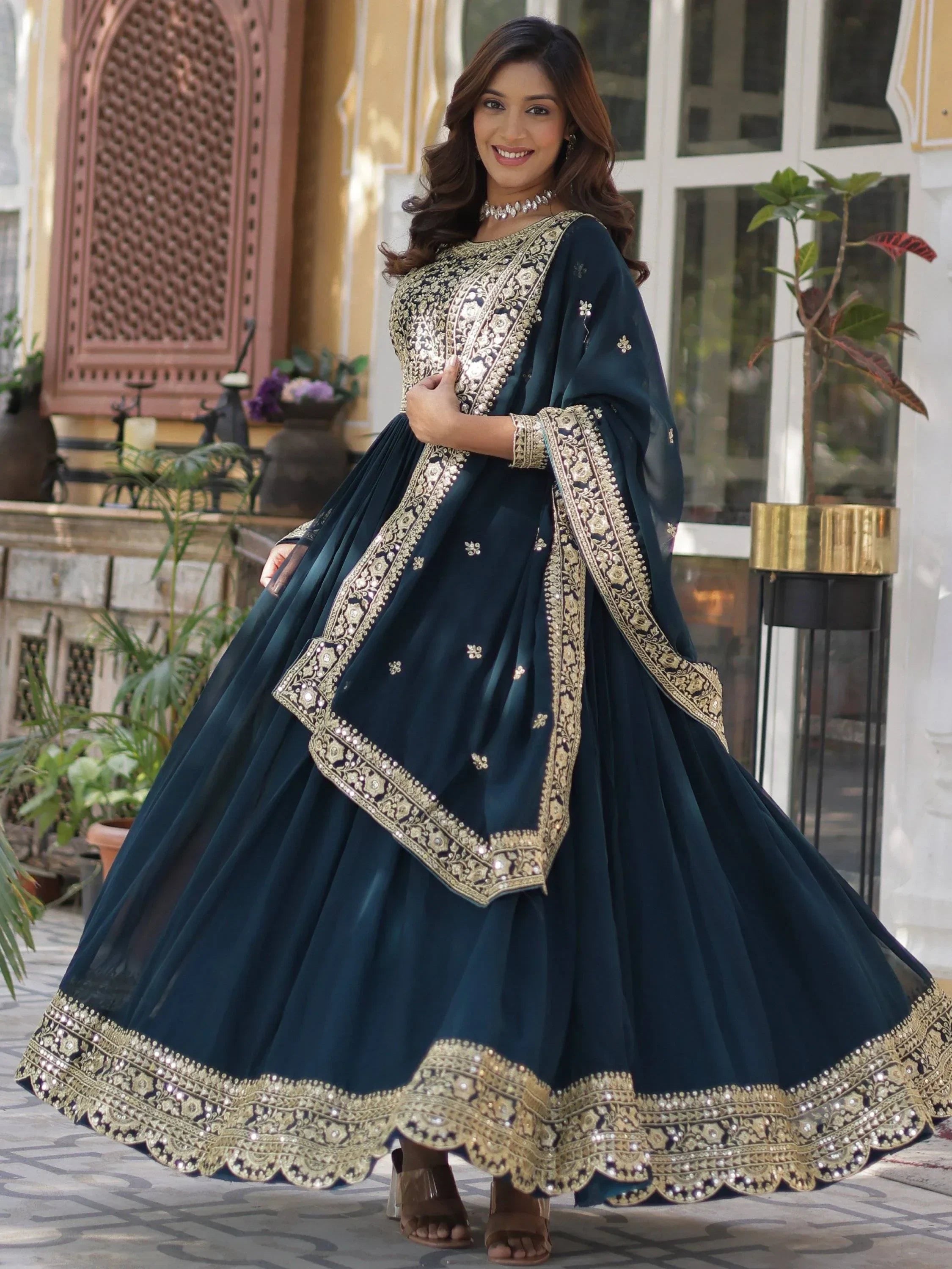 Woman in dark blue embroidered lehenga choli with gold detailing, standing outdoors.