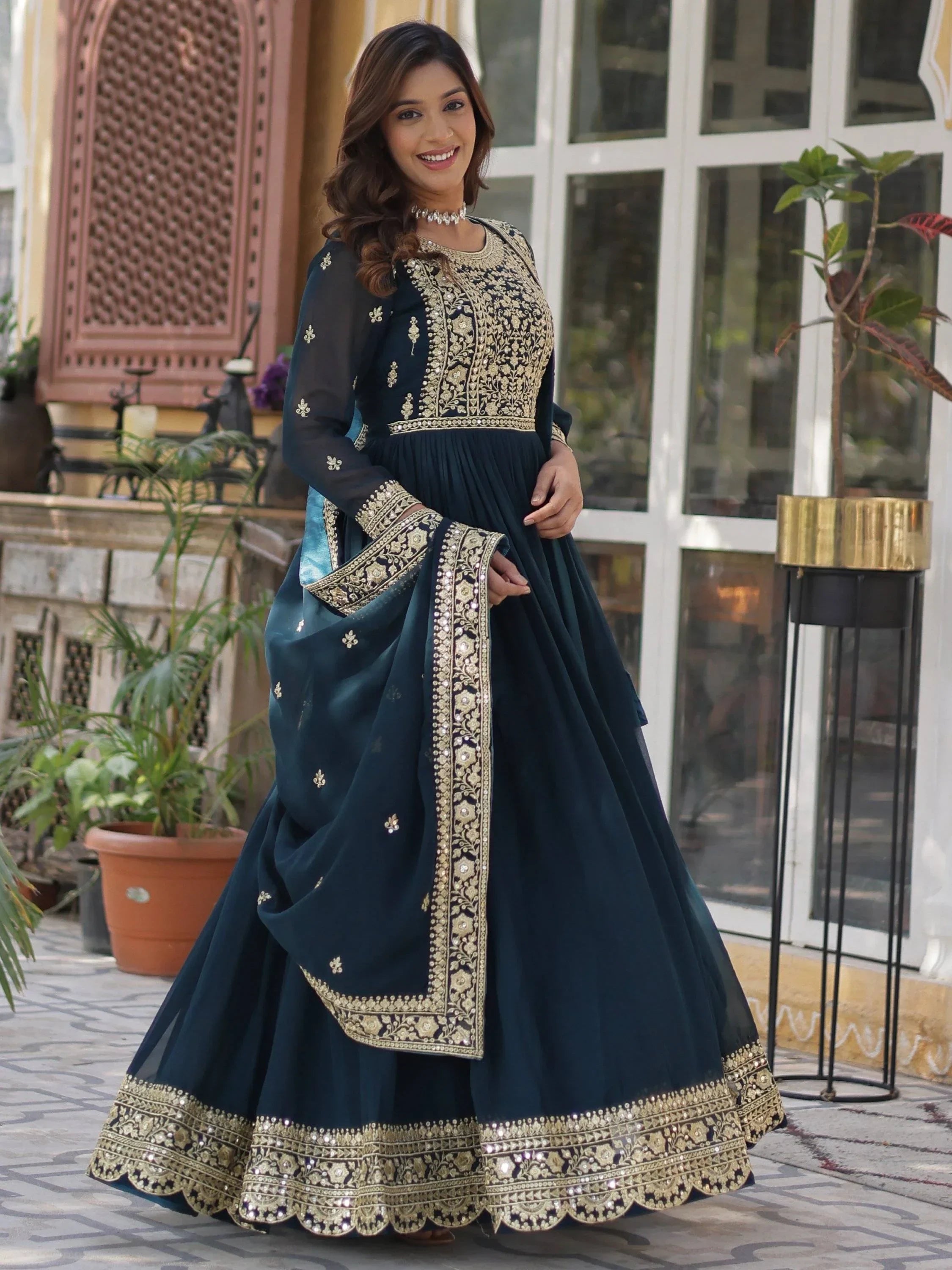 Woman wearing a navy blue embroidered Anarkali gown with gold detailing, outdoor setting
