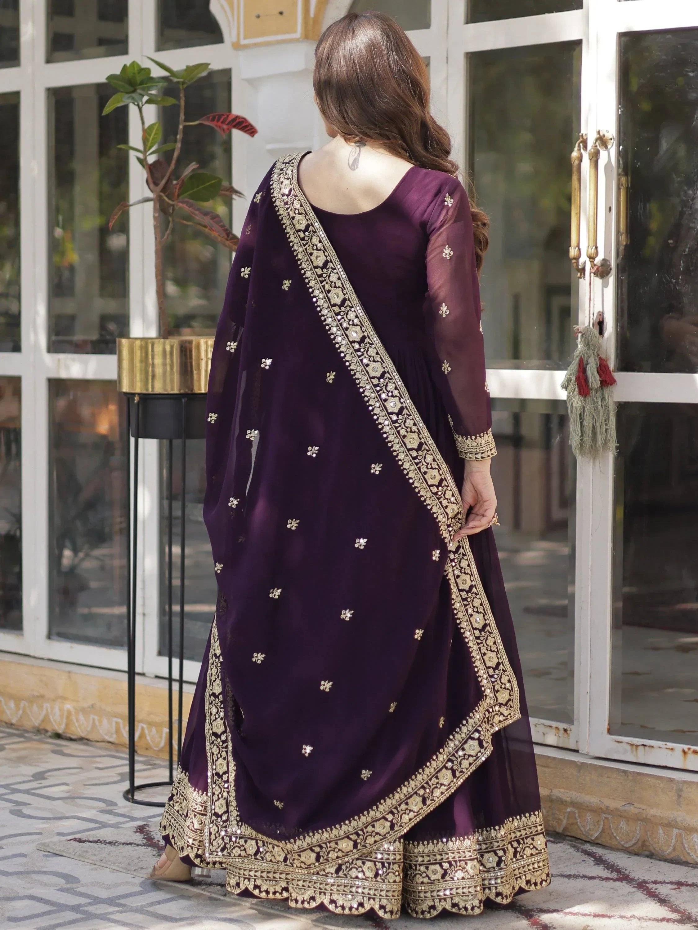 Woman wearing wine purple designer lehenga choli with gold embroidery, outdoor setting