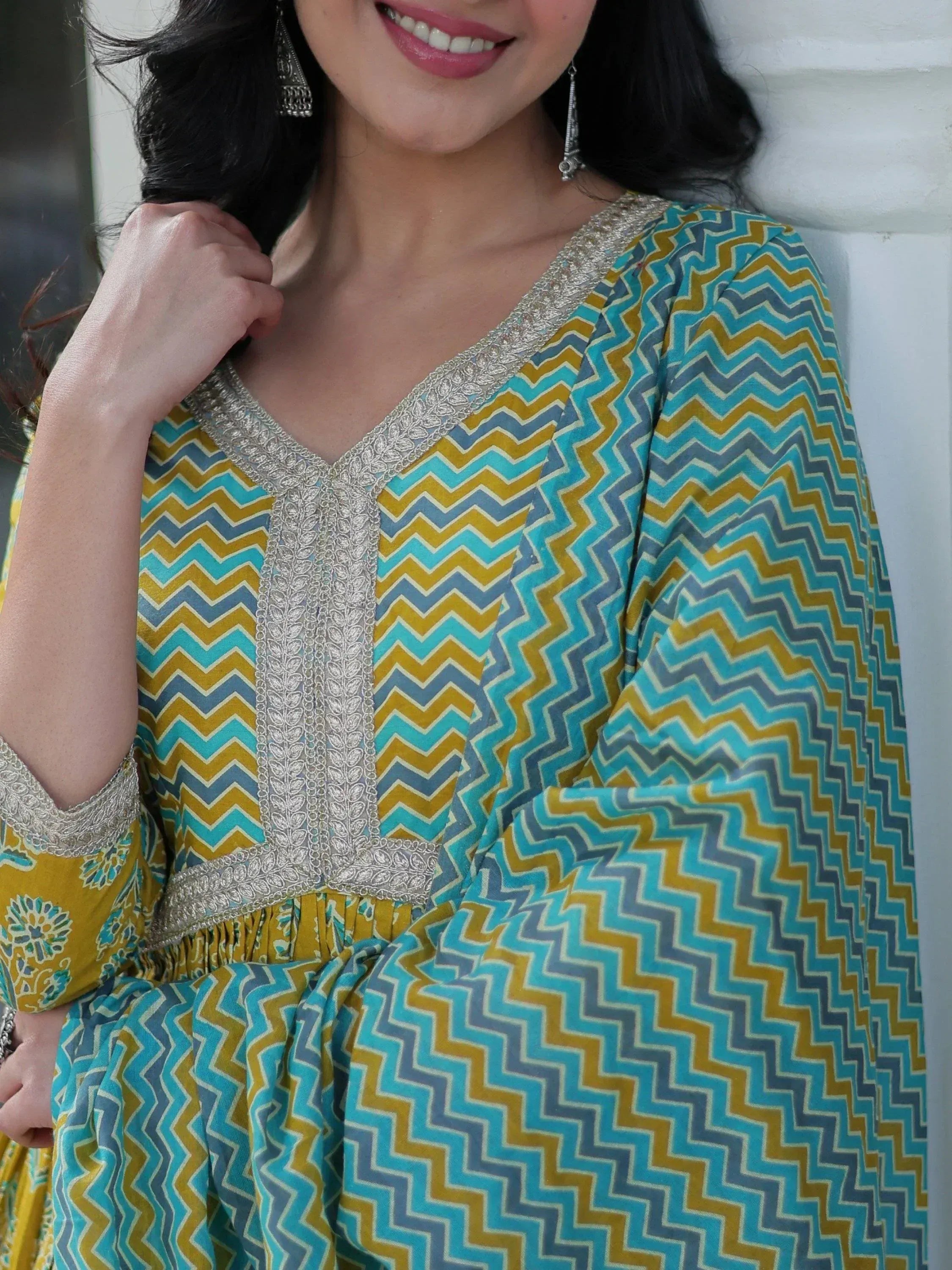 Woman in vibrant blue and yellow chevron print ethnic gown with silver embroidery, styled with jhumka earrings.
