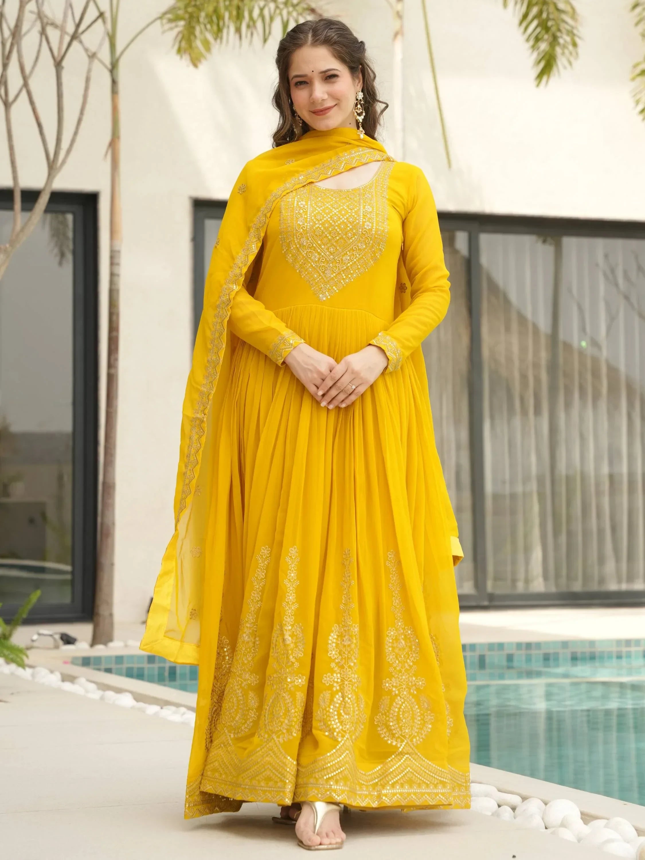 Woman wearing a yellow embroidered Anarkali suit with dupatta by a poolside