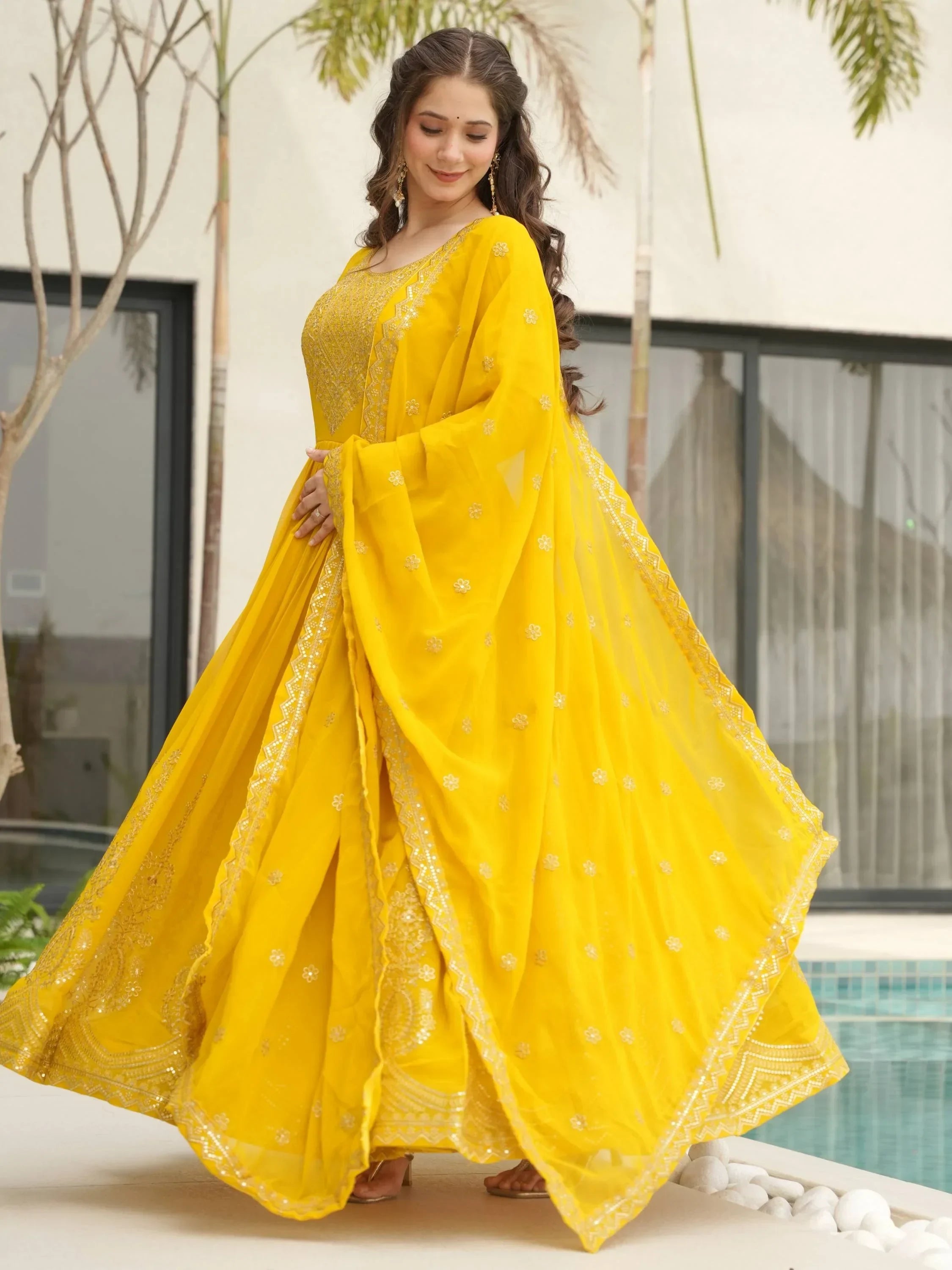 Woman in vibrant yellow embroidered lehenga choli with dupatta, outdoors by a pool