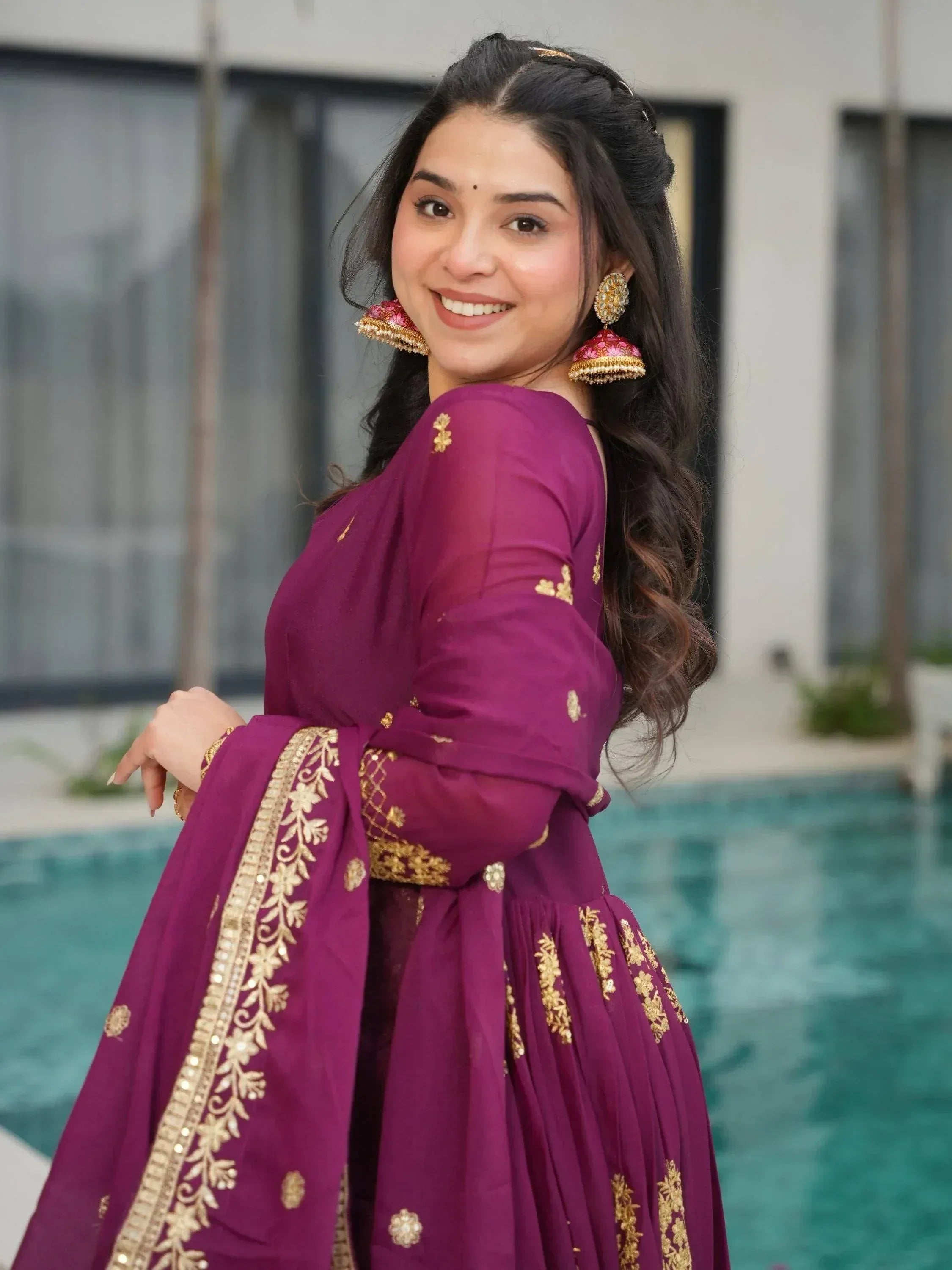 Woman in purple embroidered ethnic gown with gold detailing, standing by poolside