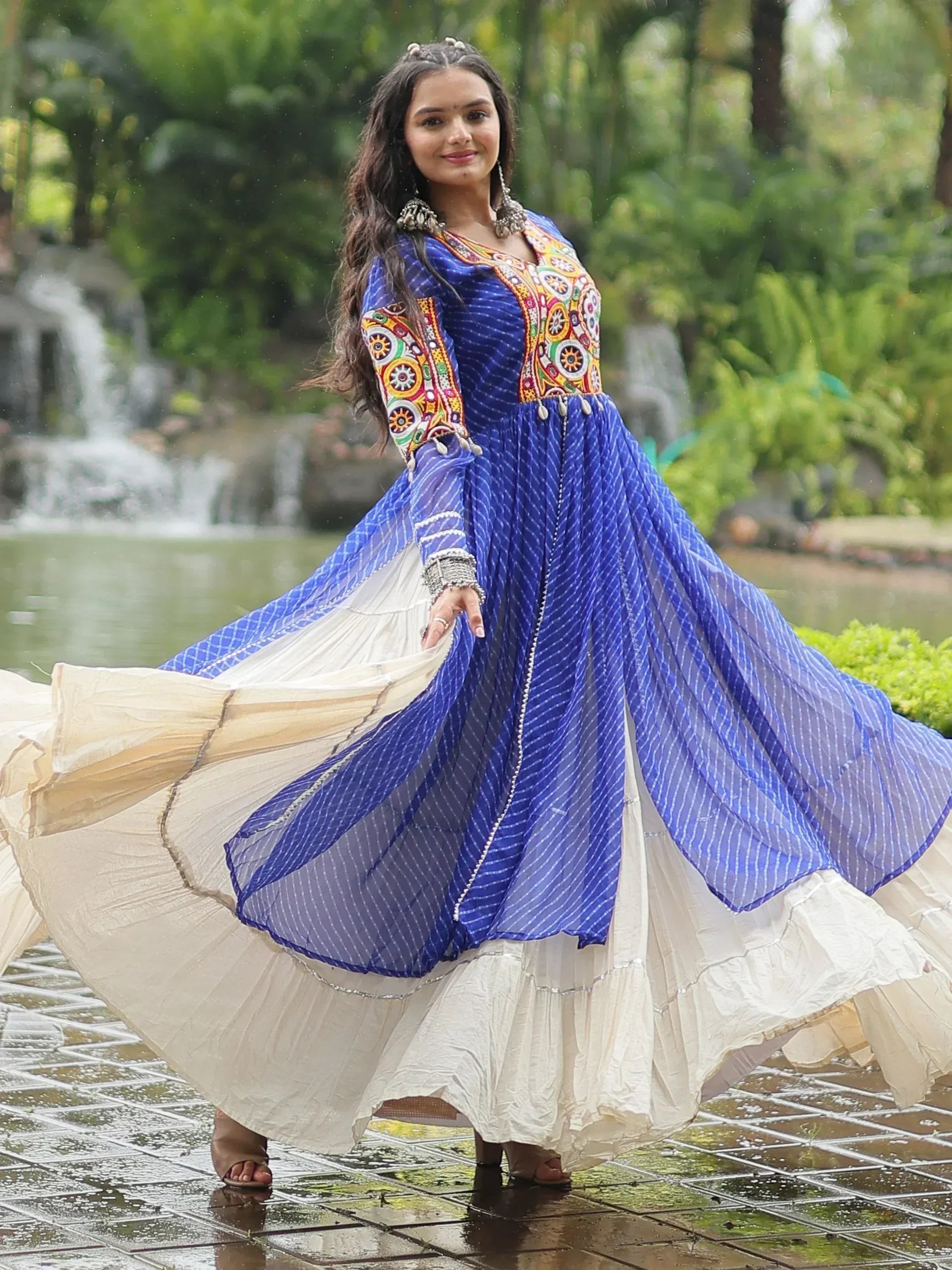 Woman in blue embroidered ethnic gown with flared skirt, dancing near waterfall