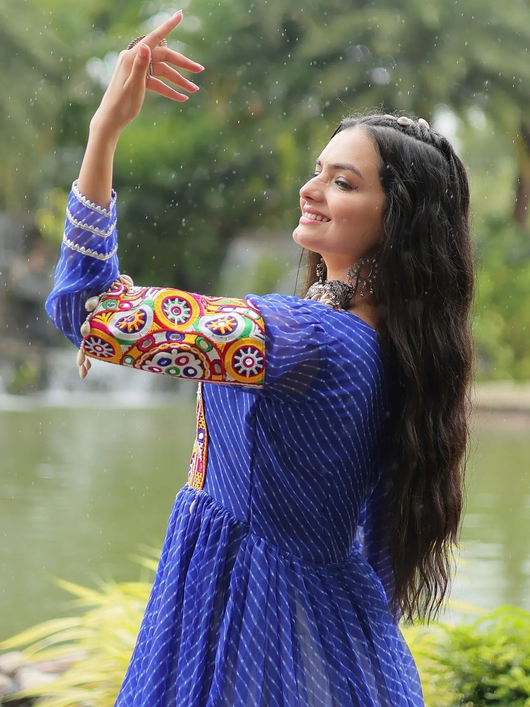 Woman in blue ethnic gown with colorful embroidery, enjoying rain outdoors
