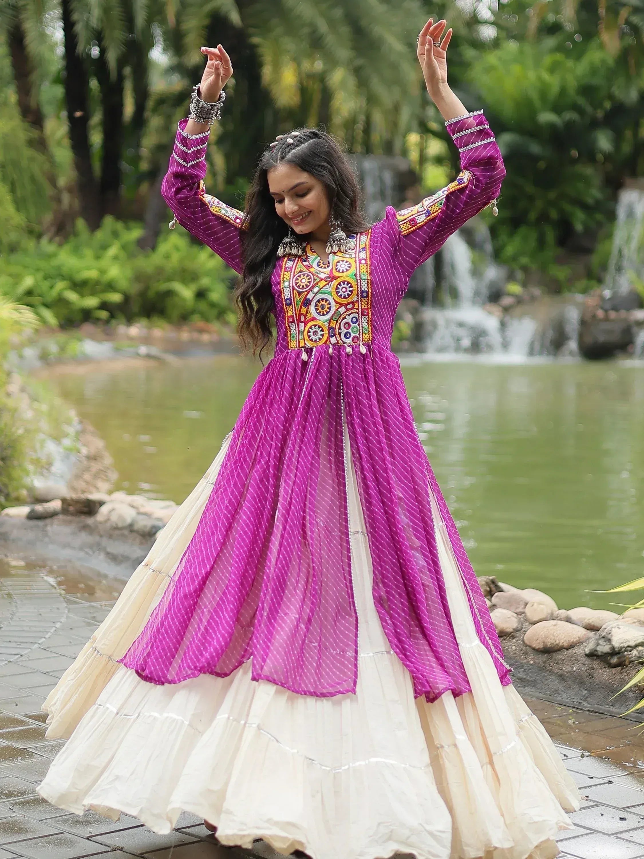 Woman in purple embroidered ethnic gown with cream skirt by a pond and greenery