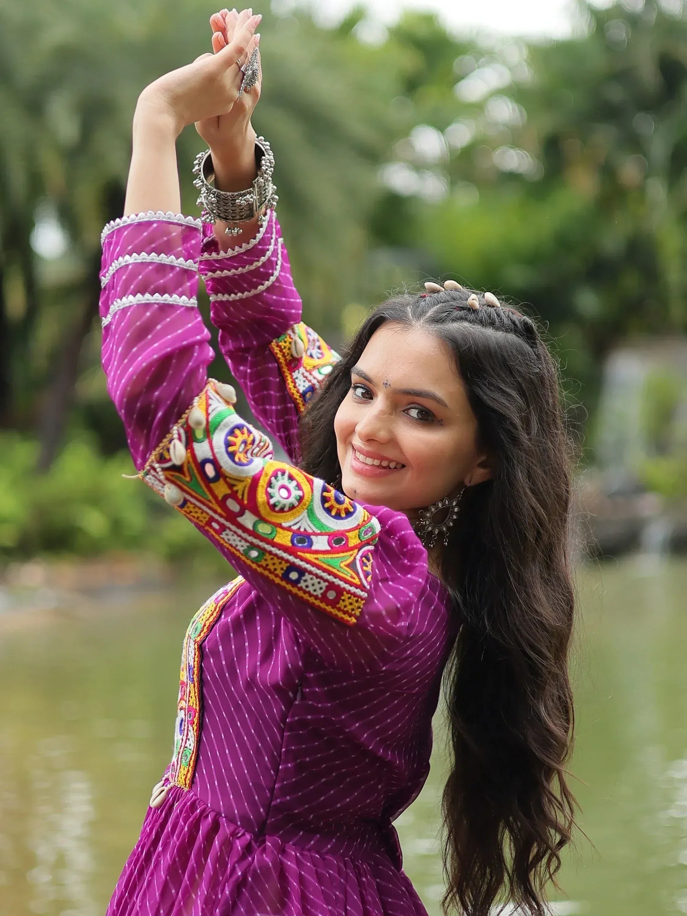 Woman in purple embroidered Indian ethnic dress with silver bangles by a lake