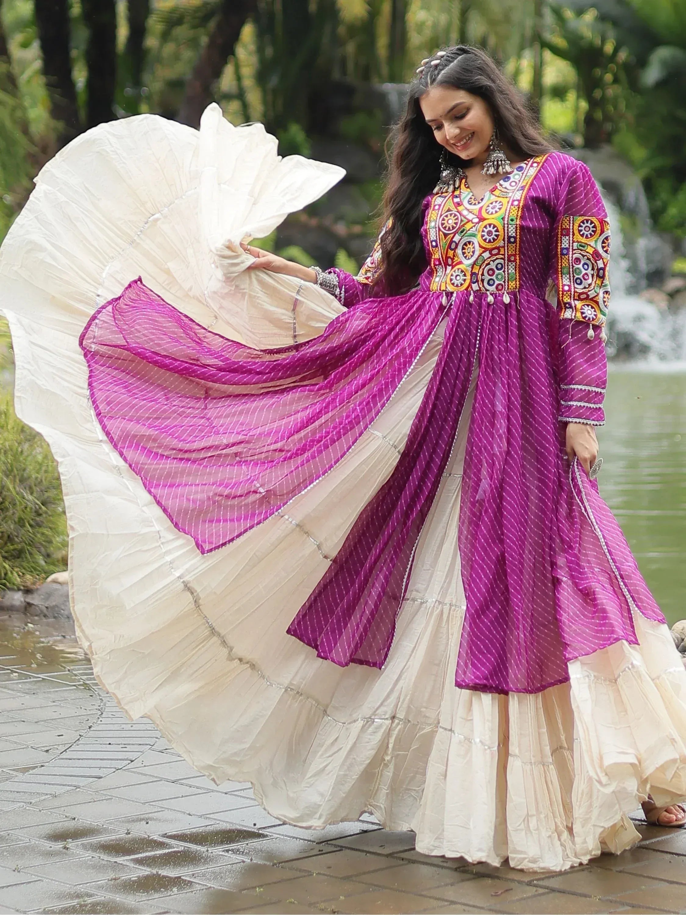 Woman in outdoor setting wearing a traditional wine purple embroidered Anarkali gown with cream flare skirt