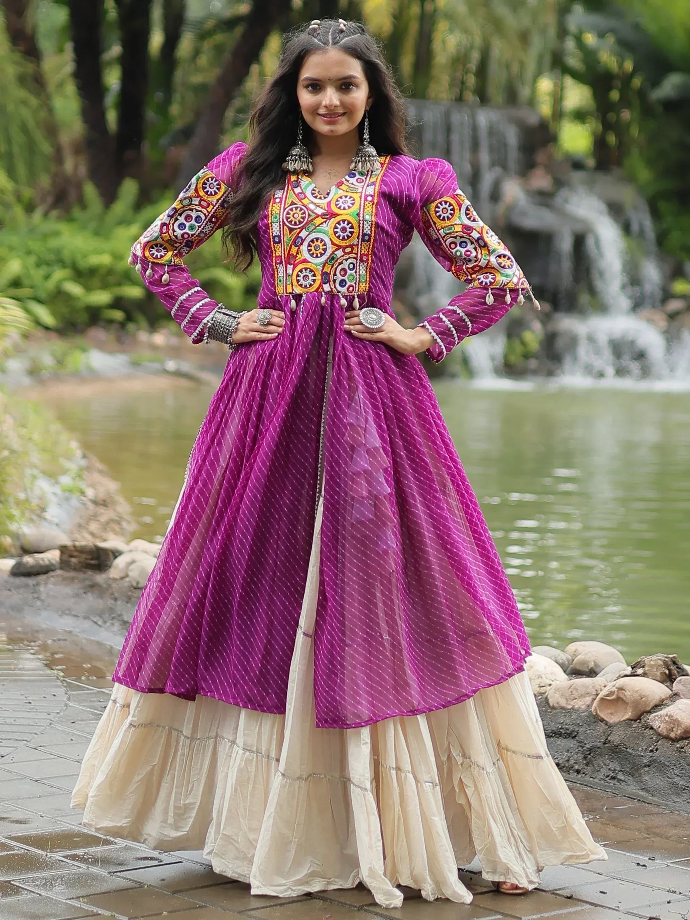 Woman in wine and cream embroidered Anarkali gown with mirror work, outdoors by waterfall