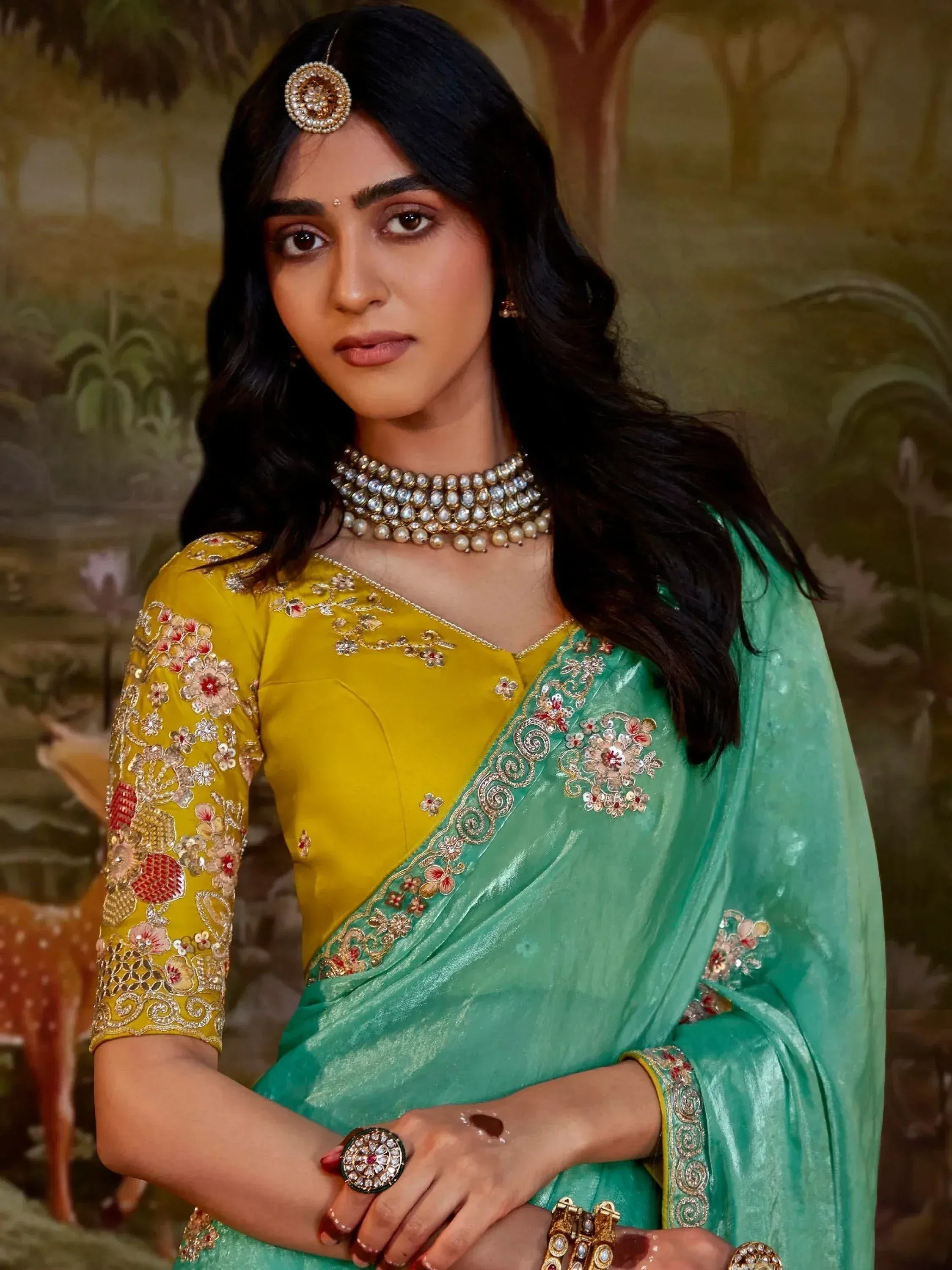 Woman in yellow and green embroidered saree with floral designs and traditional jewelry
