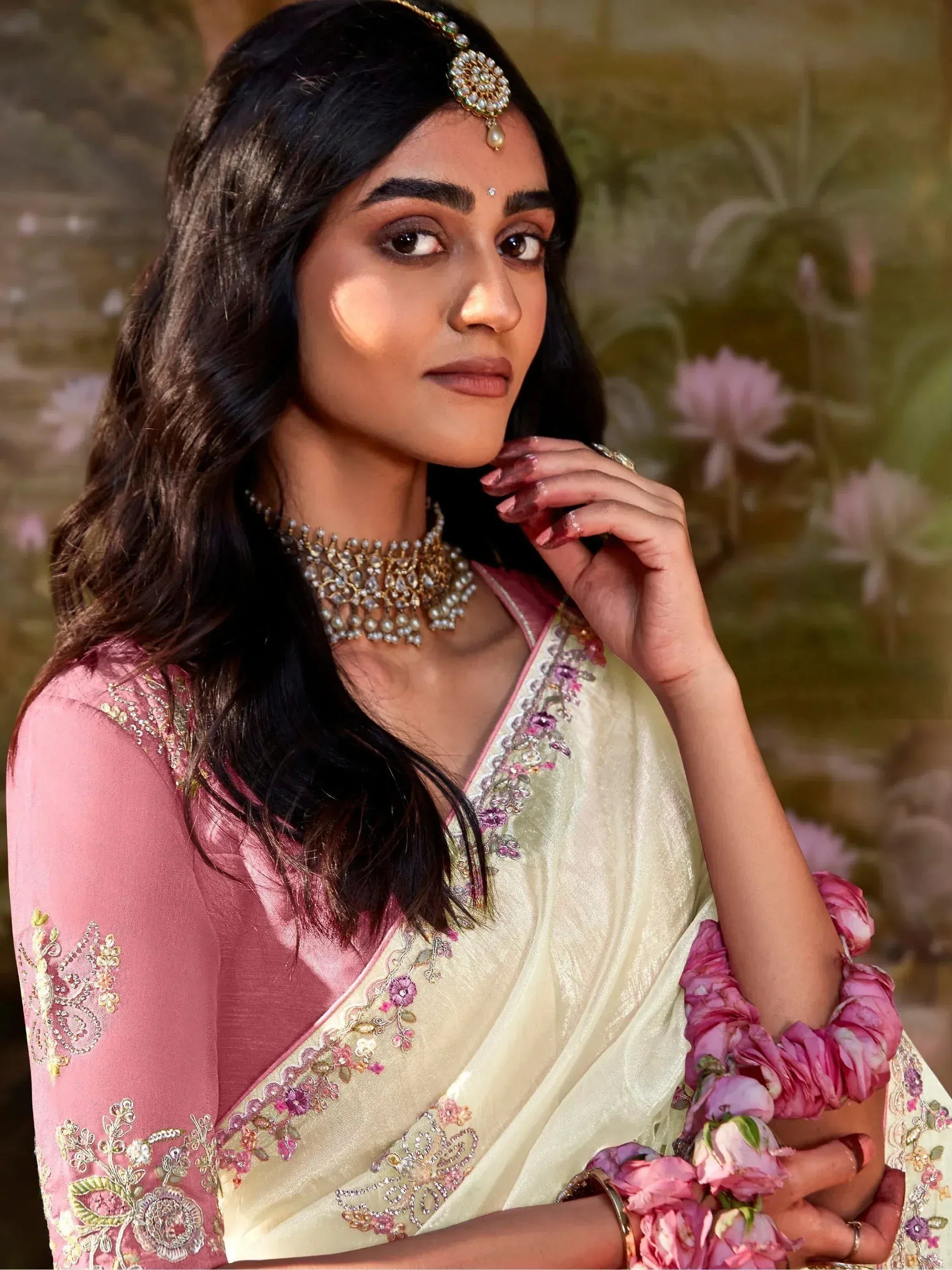 Woman in elegant pink and cream embroidered saree with floral details and traditional jewelry