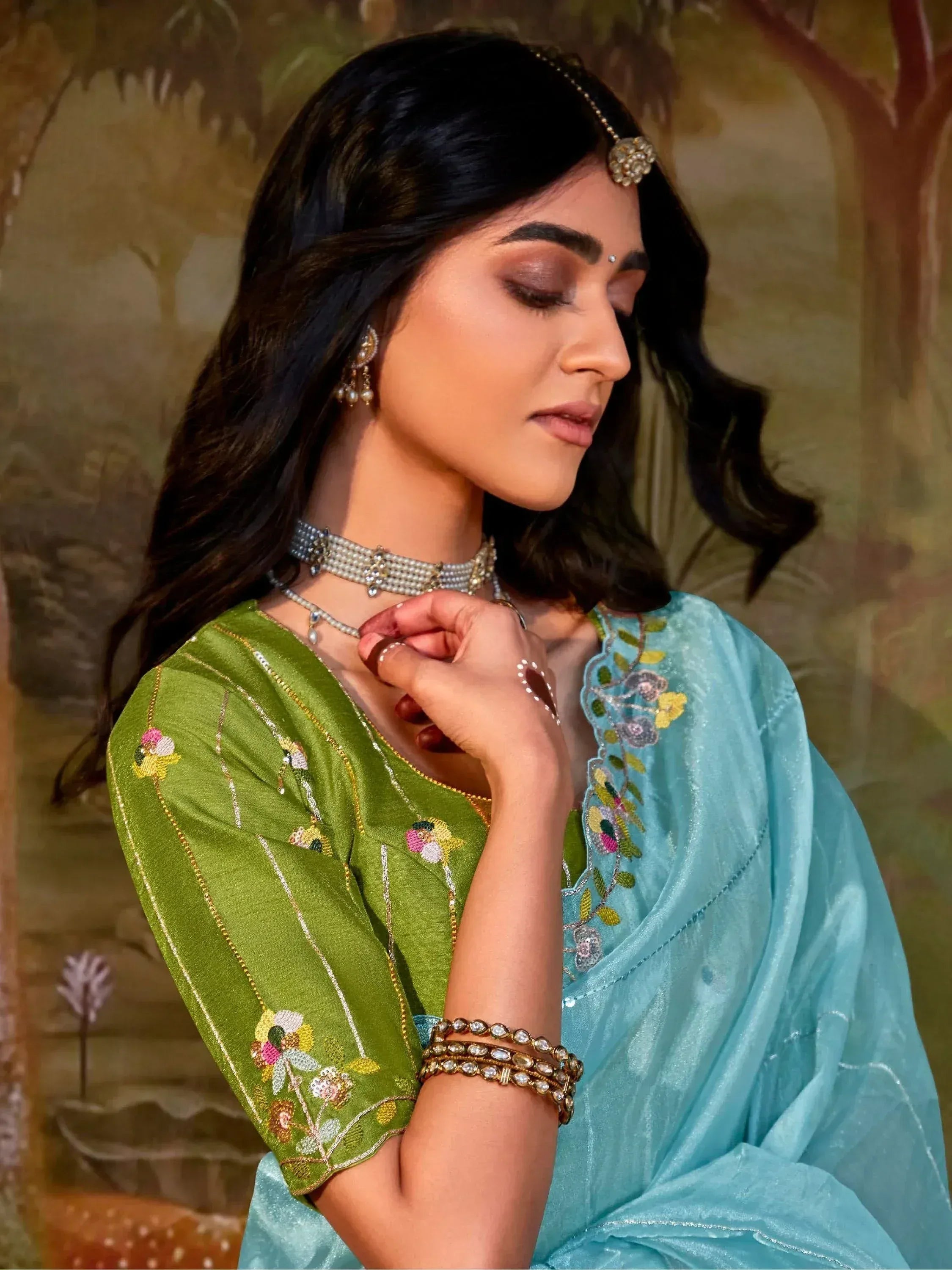 Woman in green embroidered blouse and blue saree with traditional jewelry, perfect for Indian ethnic wear occasions