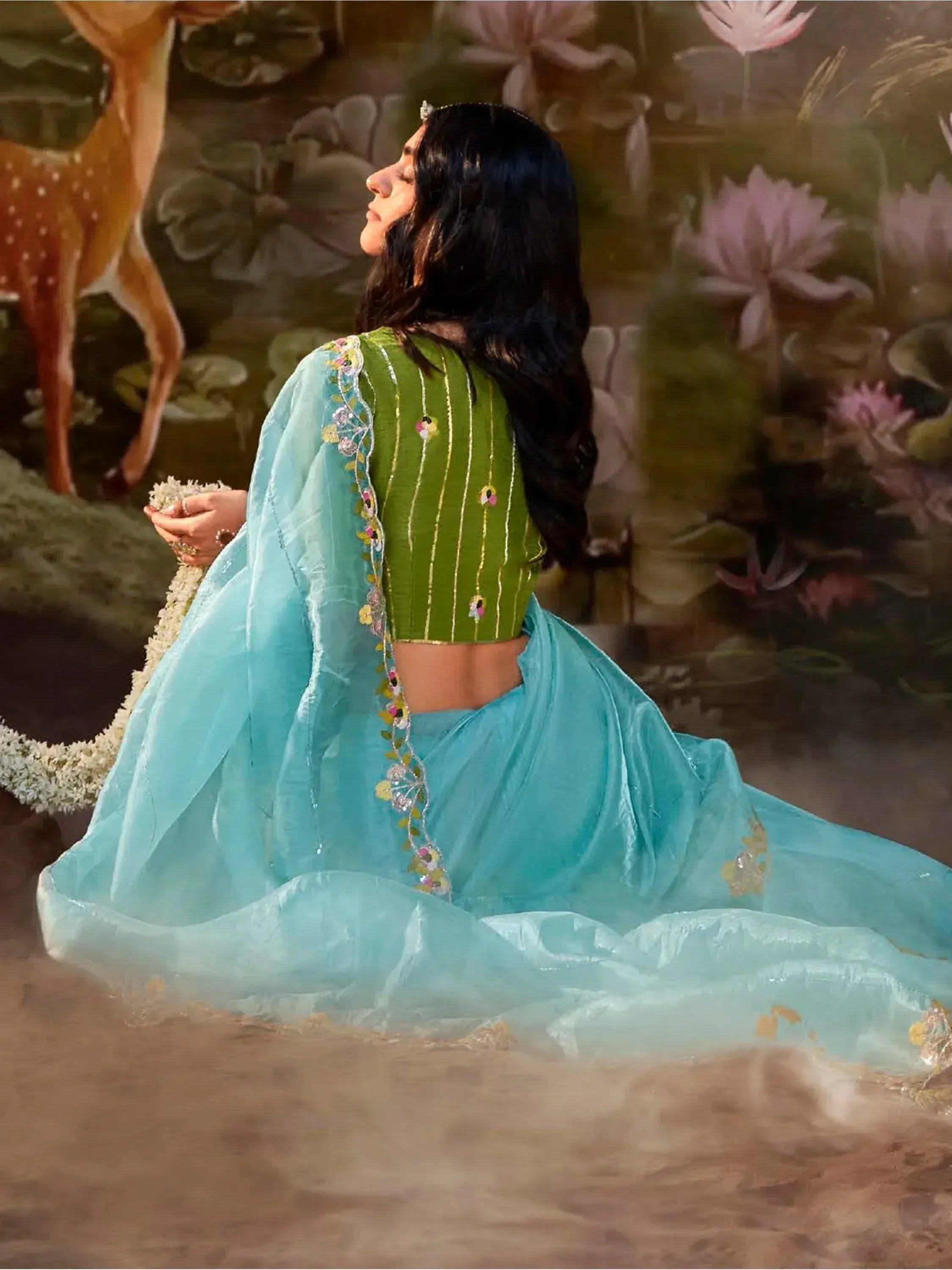 Woman in green embroidered blouse and turquoise saree with floral border, ideal for Indian ethnic wear occasions.
