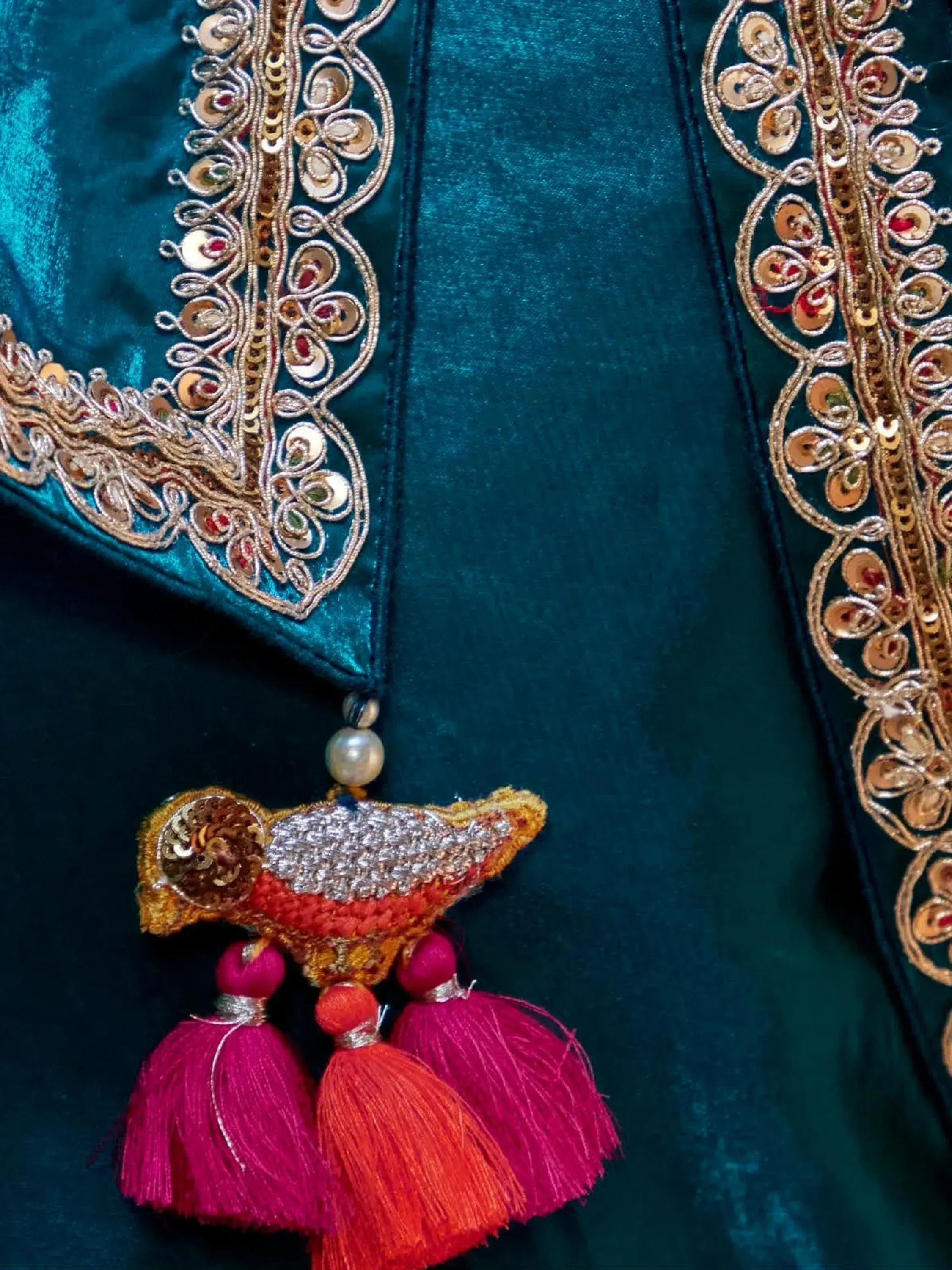Teal velvet ethnic wear with gold embroidery, sequins, and colorful bird tassel detail