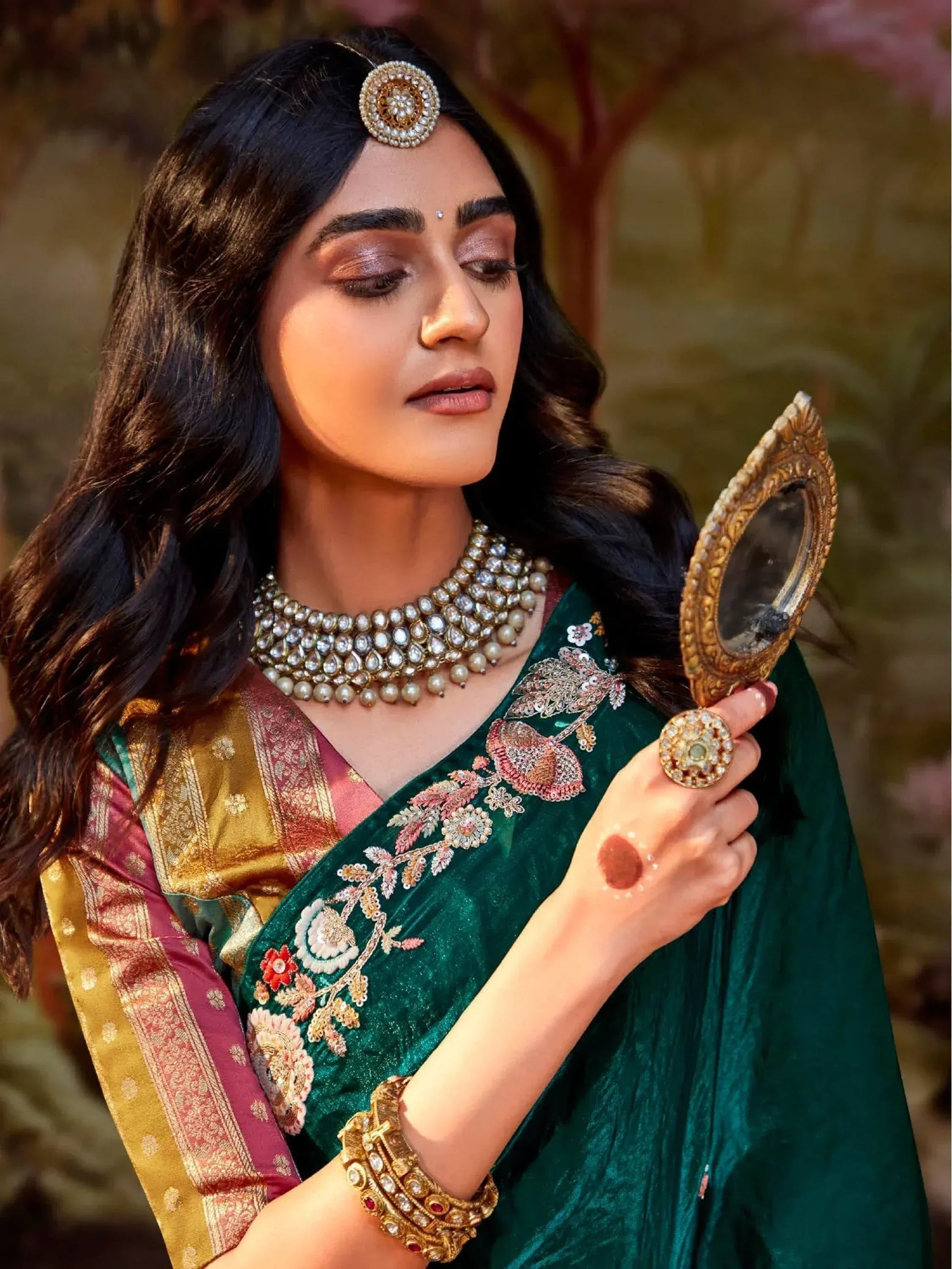 Woman in green embroidered saree with gold jewelry holding vintage mirror, Indian ethnic wear