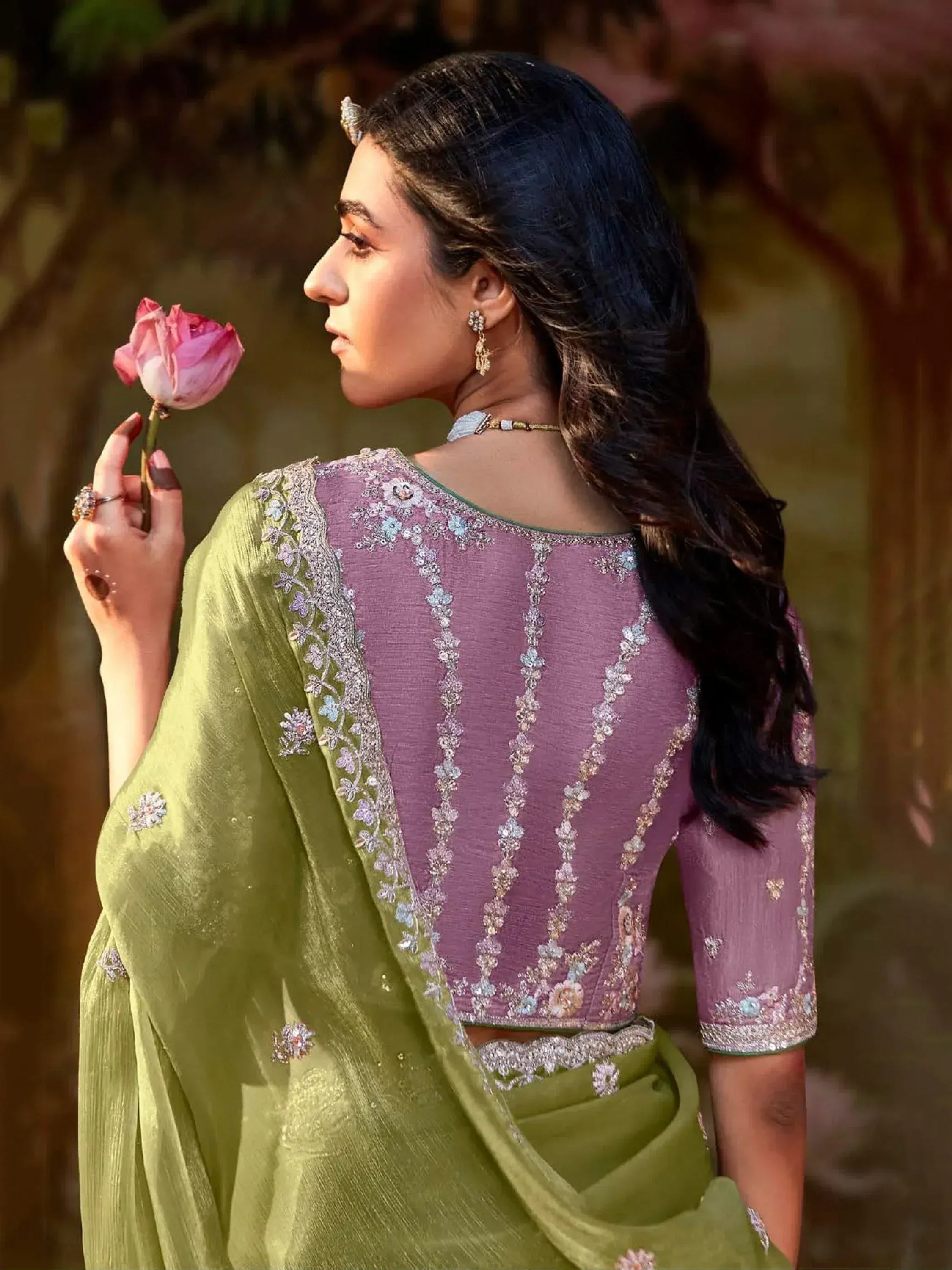 Woman in purple embroidered blouse with green saree, holding pink rose, Indian ethnic wear