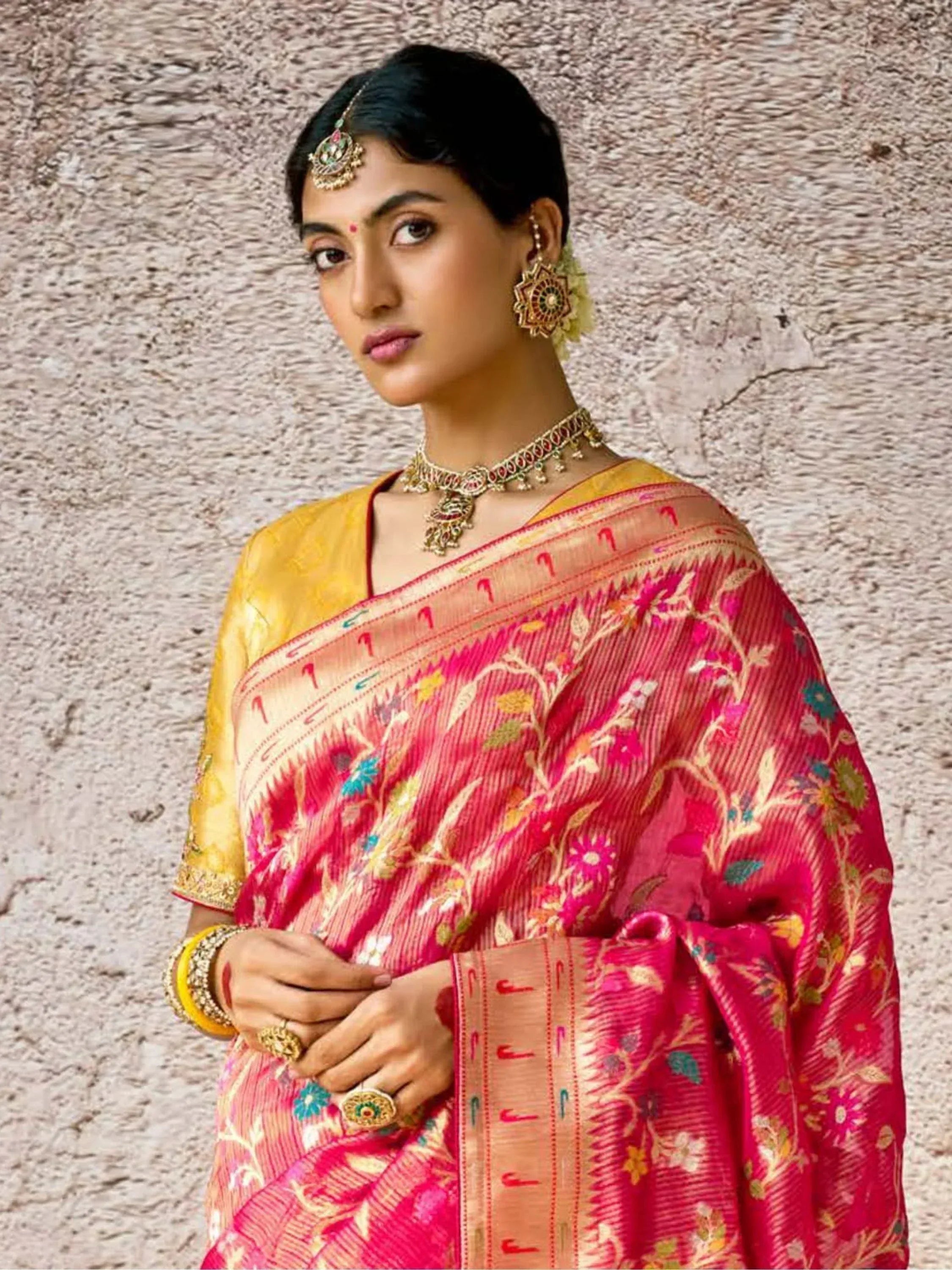 Woman in vibrant pink floral saree with gold blouse, traditional Indian jewelry, and ethnic makeup