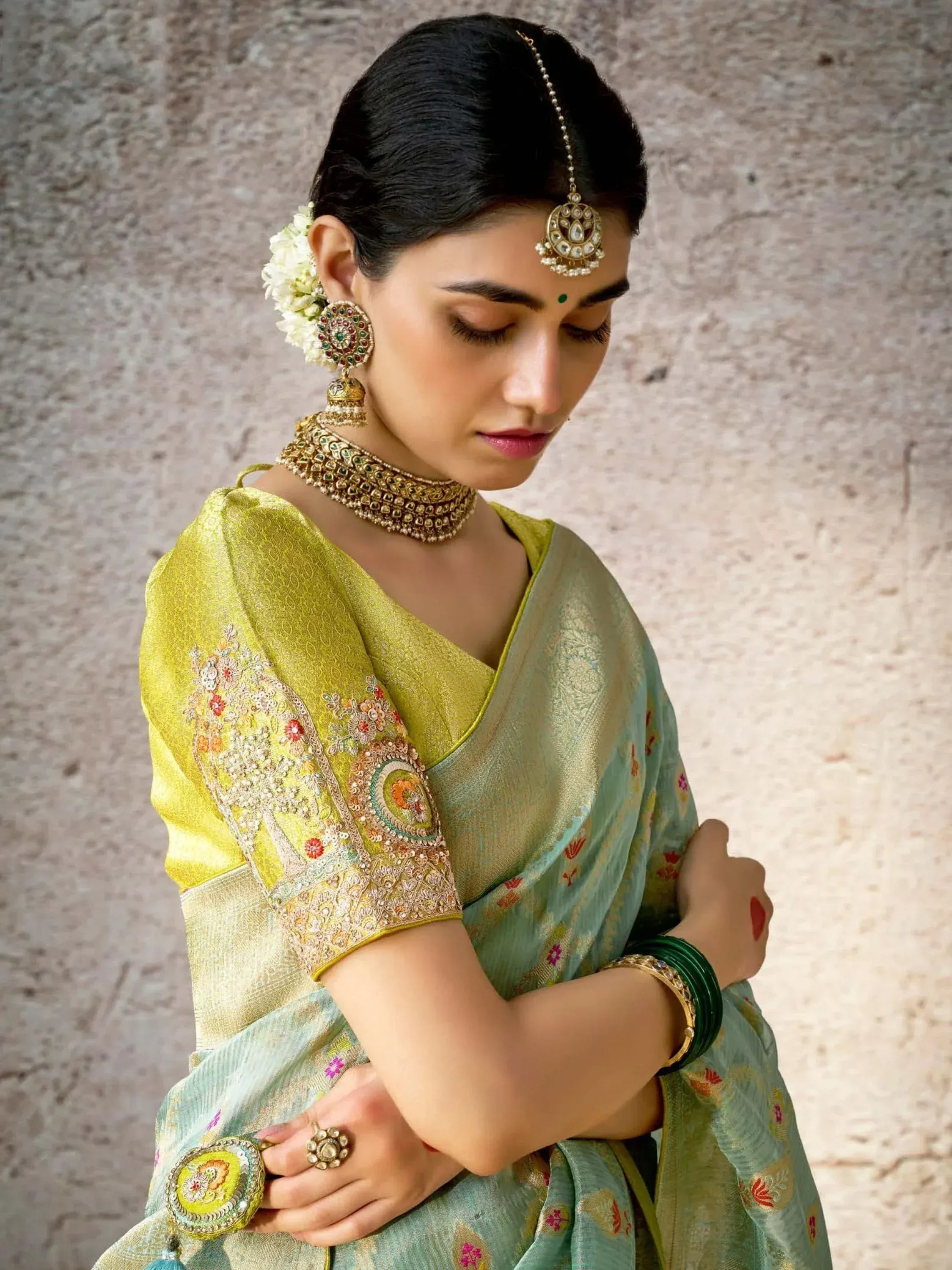 Woman in elegant green and yellow embroidered saree with traditional Indian jewelry and floral hair accessory