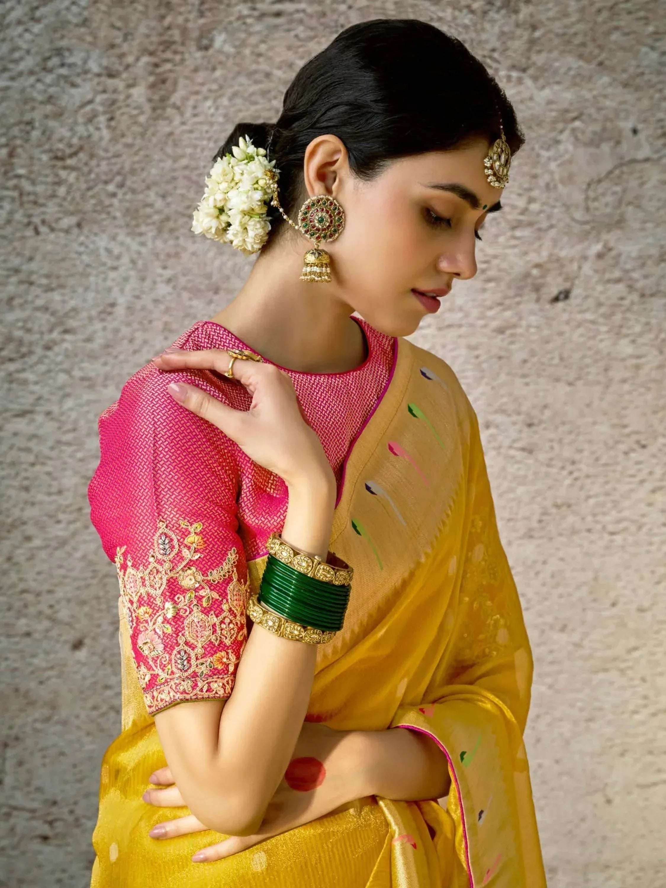 Woman in yellow saree with pink embroidered blouse, floral hair accessory, and traditional jewelry