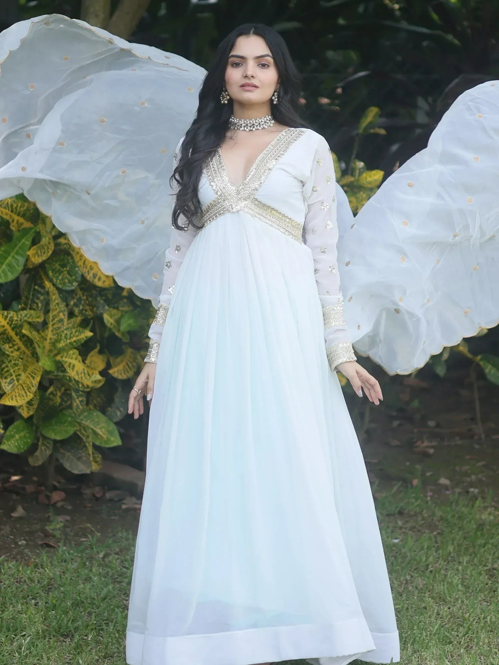Elegant white ethnic gown with gold embroidery, sheer sleeves, and dramatic cape for Indian occasions