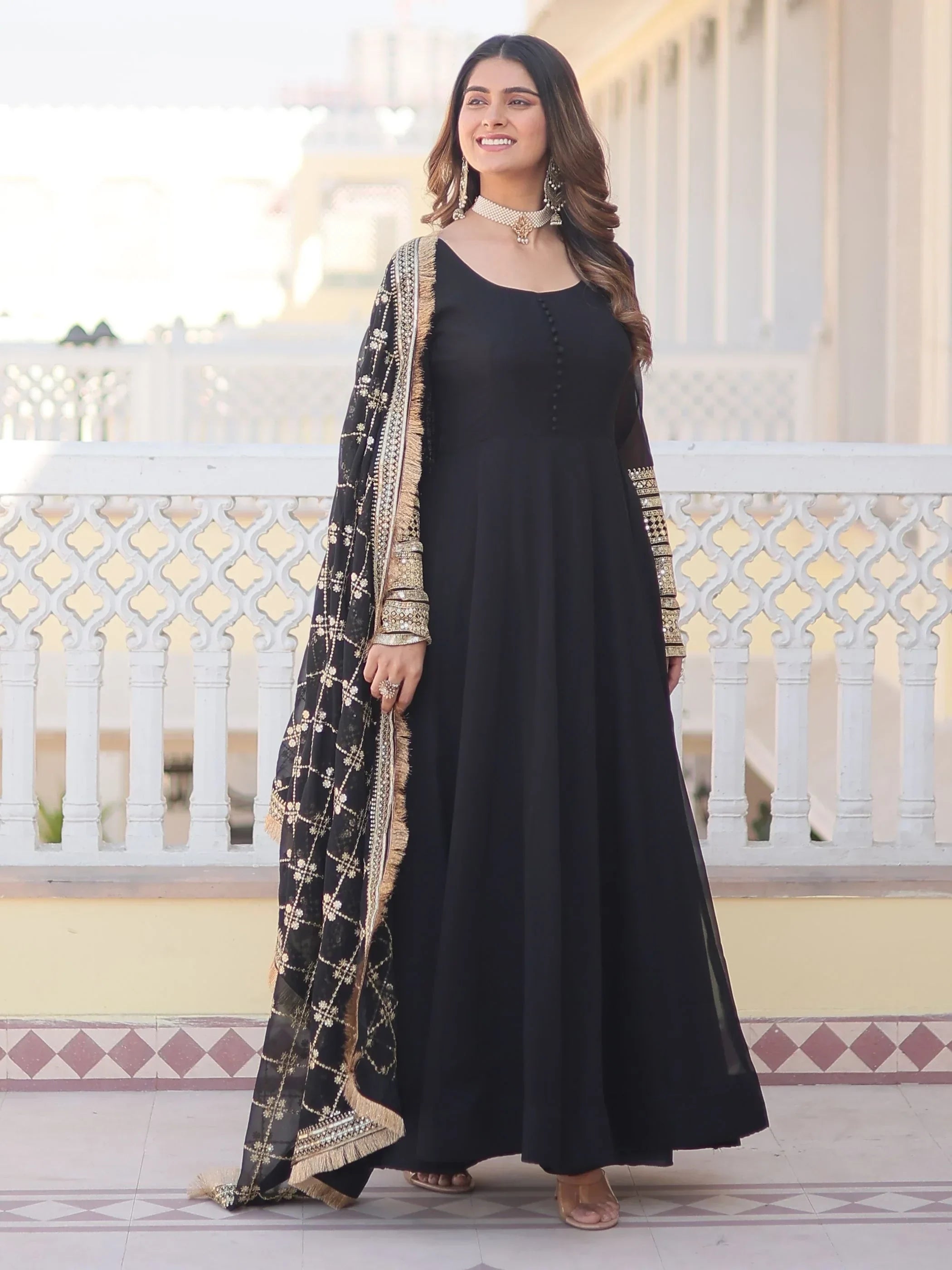 Woman wearing black embroidered ethnic gown with gold dupatta, standing outdoors