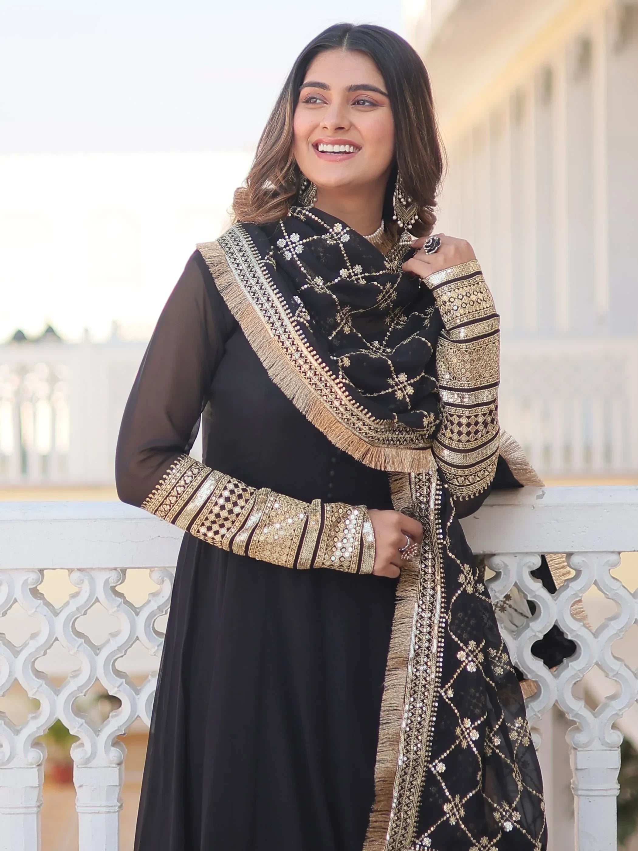 Woman in black and gold embroidered ethnic gown with dupatta, smiling outdoors