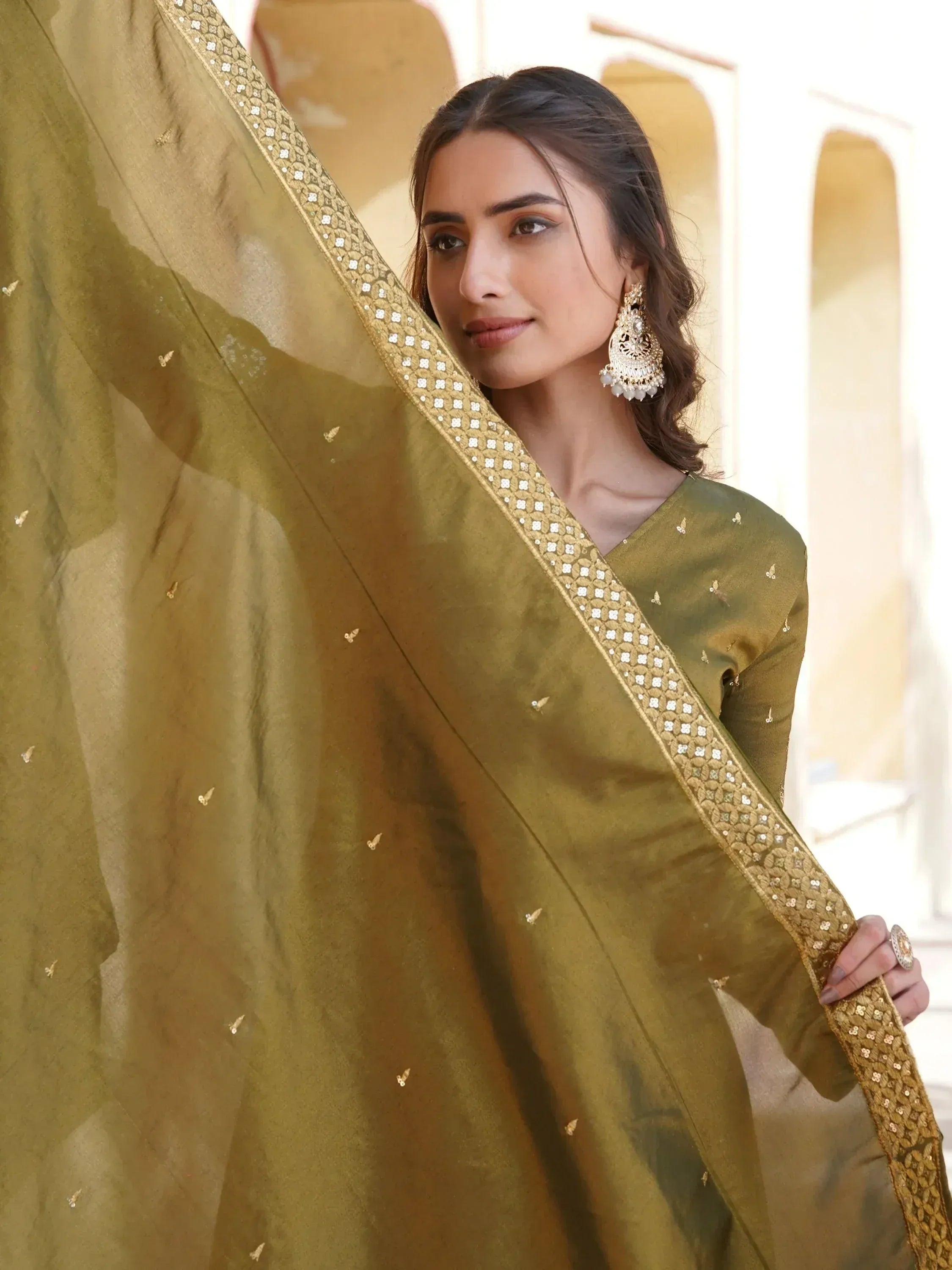 Olive green saree with gold sequin border and butterfly motifs, styled with statement earrings