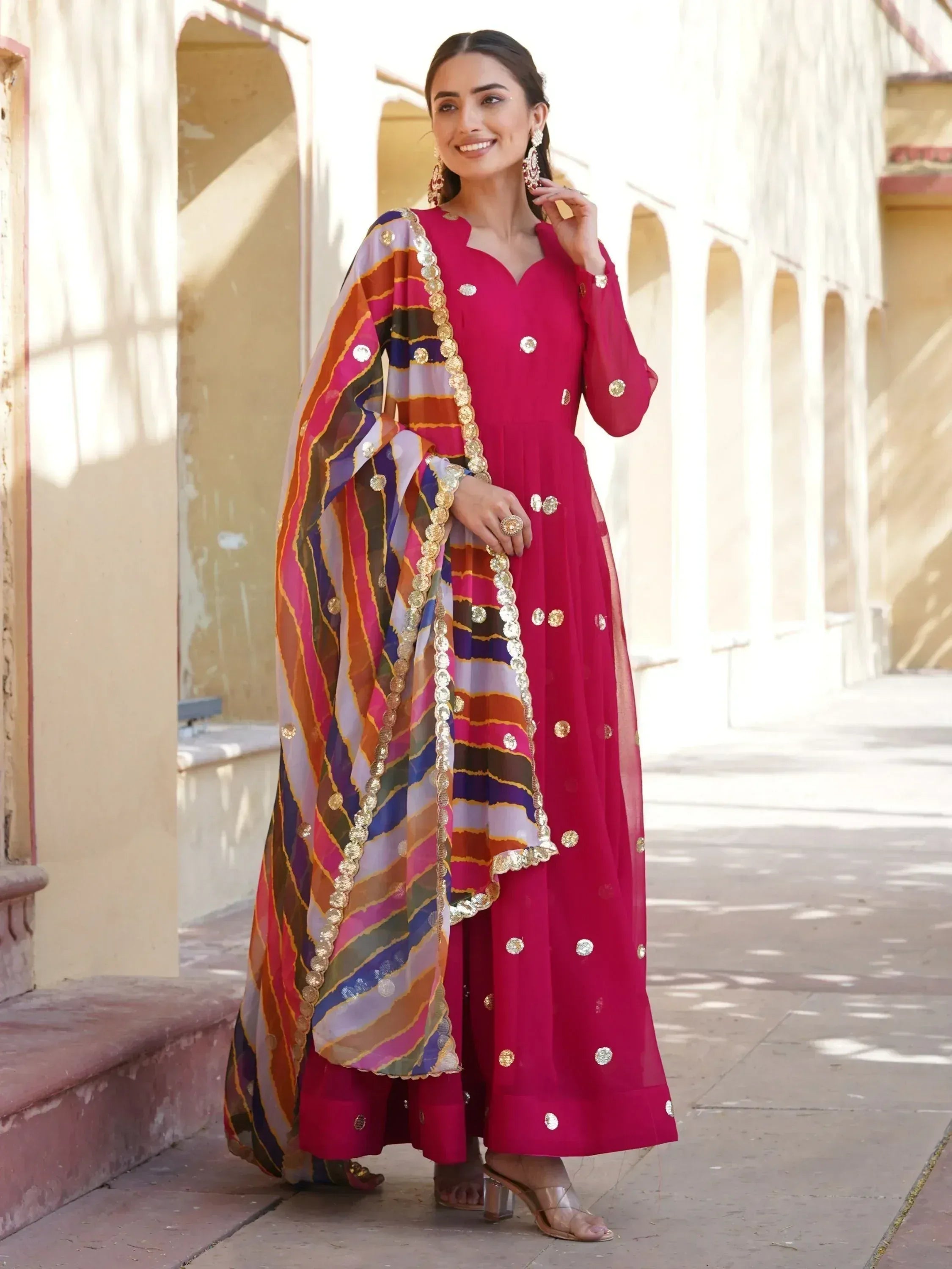 Woman in vibrant pink ethnic anarkali with colorful striped dupatta, gold embellishments, perfect for Indian festive occasions.