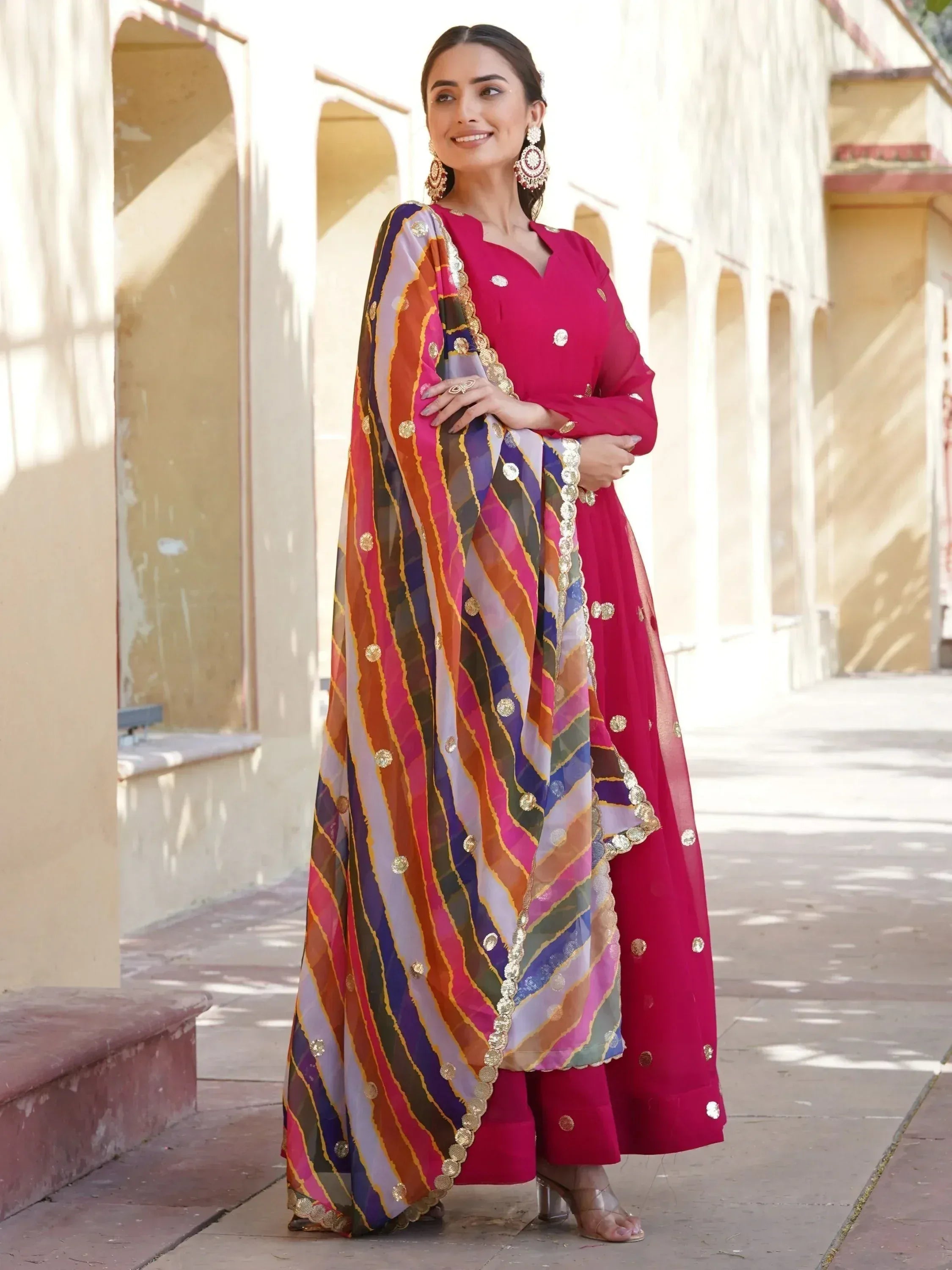 Woman in vibrant pink Indian ethnic wear with colorful striped dupatta, perfect for festive occasions.