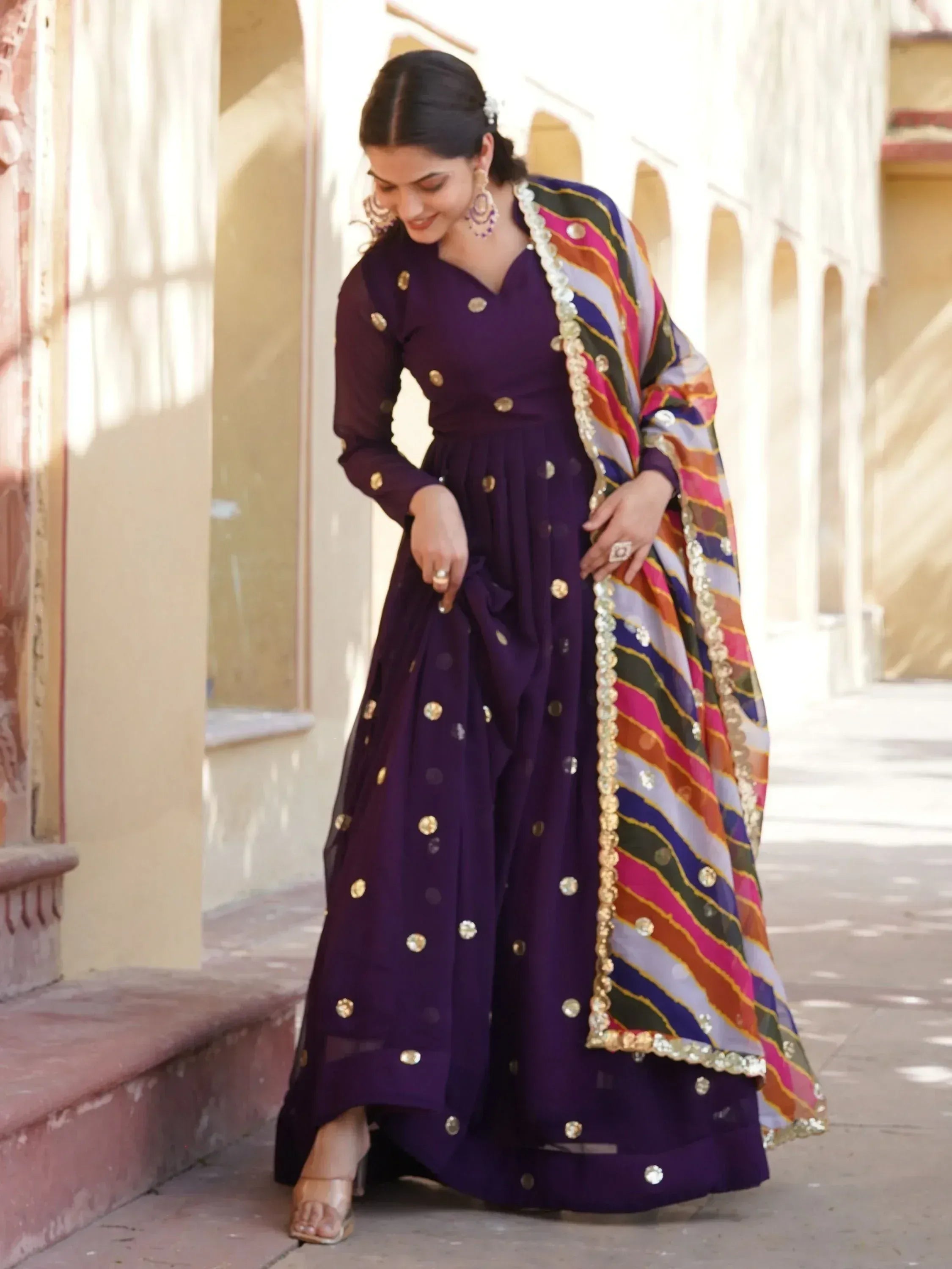 Purple ethnic gown with gold embellishments and colorful striped dupatta, perfect for Indian occasions