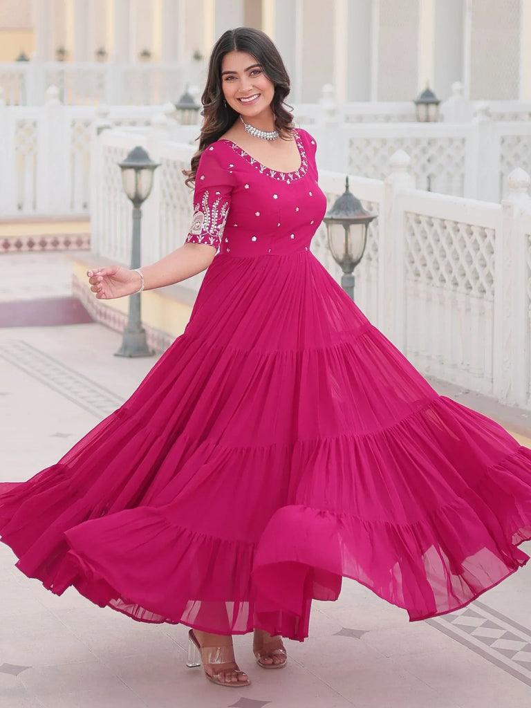 Woman in vibrant pink ethnic gown with embroidery, twirling outdoors