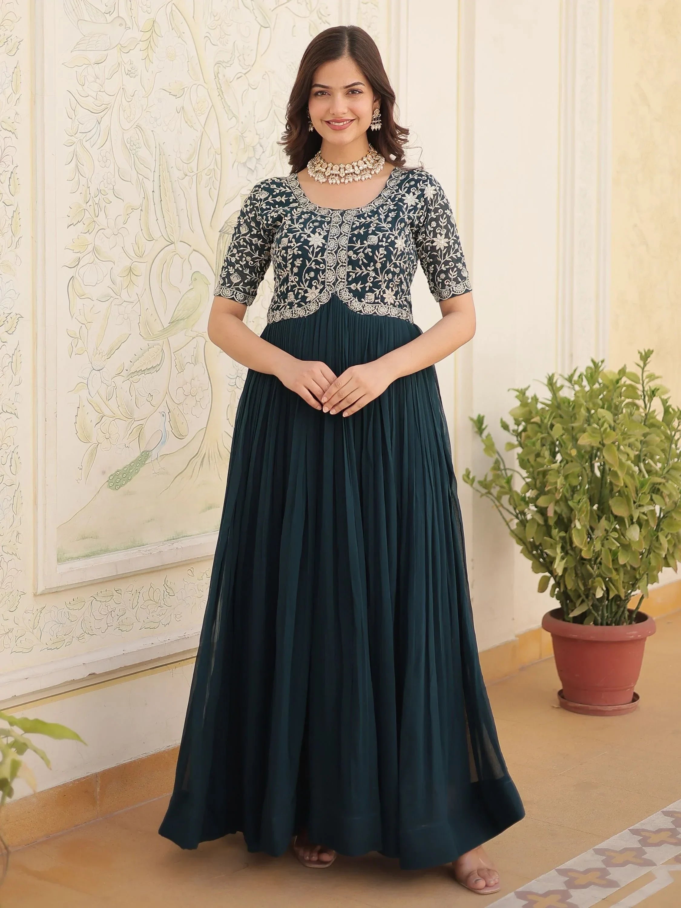 Woman in navy blue ethnic gown with embroidered bodice, standing indoors, traditional jewelry