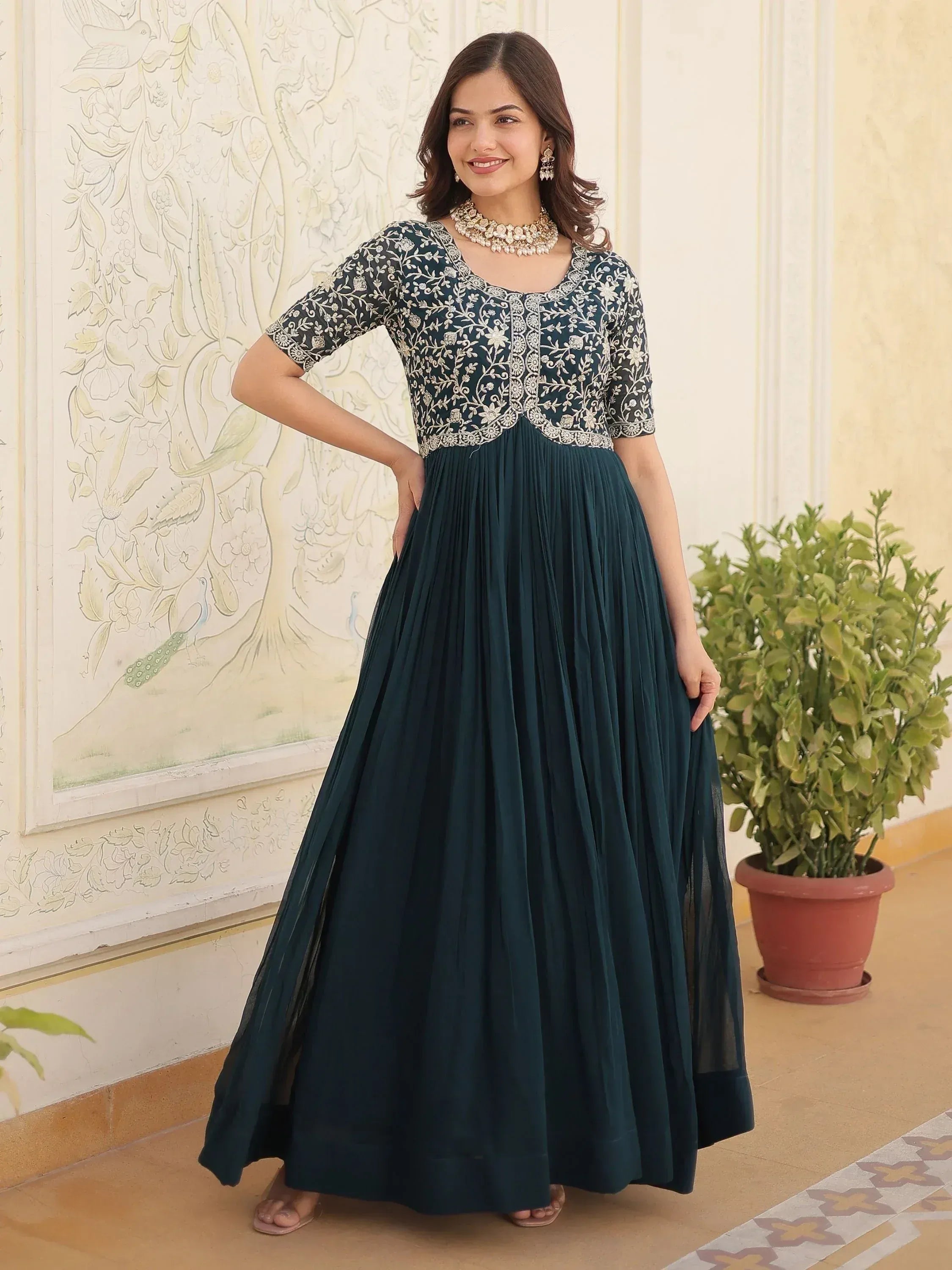 Dark green ethnic gown with floral embroidery, pleated skirt, and gold jewelry for Indian occasions