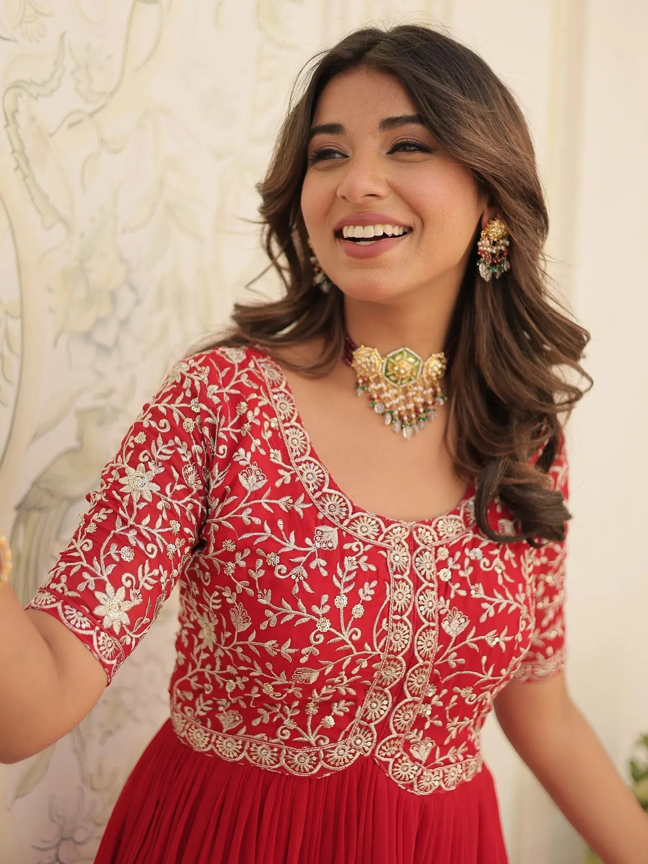 Red embroidered ethnic gown with gold floral detailing, paired with traditional jewelry for festive occasions.