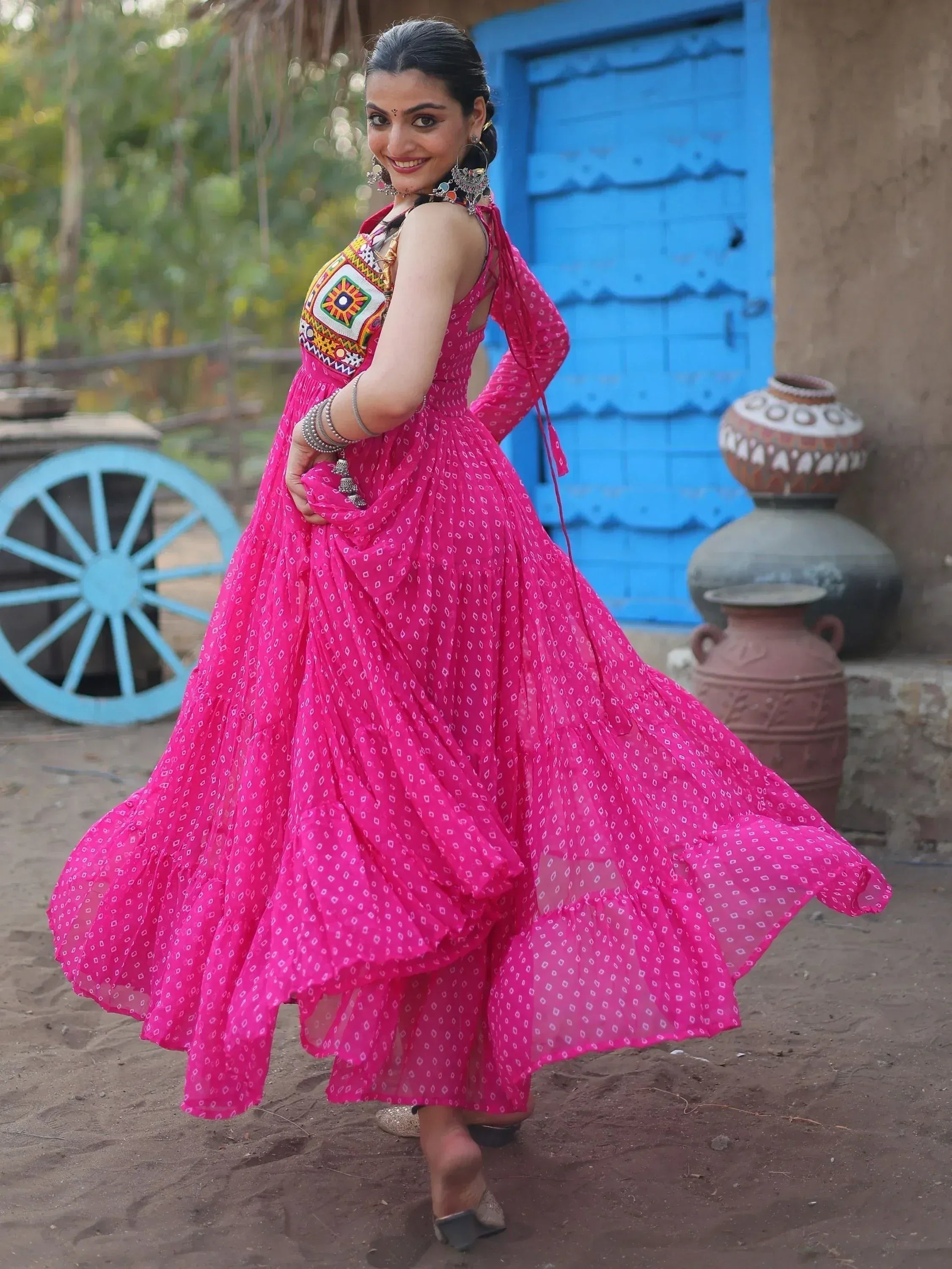 Woman in vibrant pink ethnic gown with mirror work, twirling outdoors near blue door