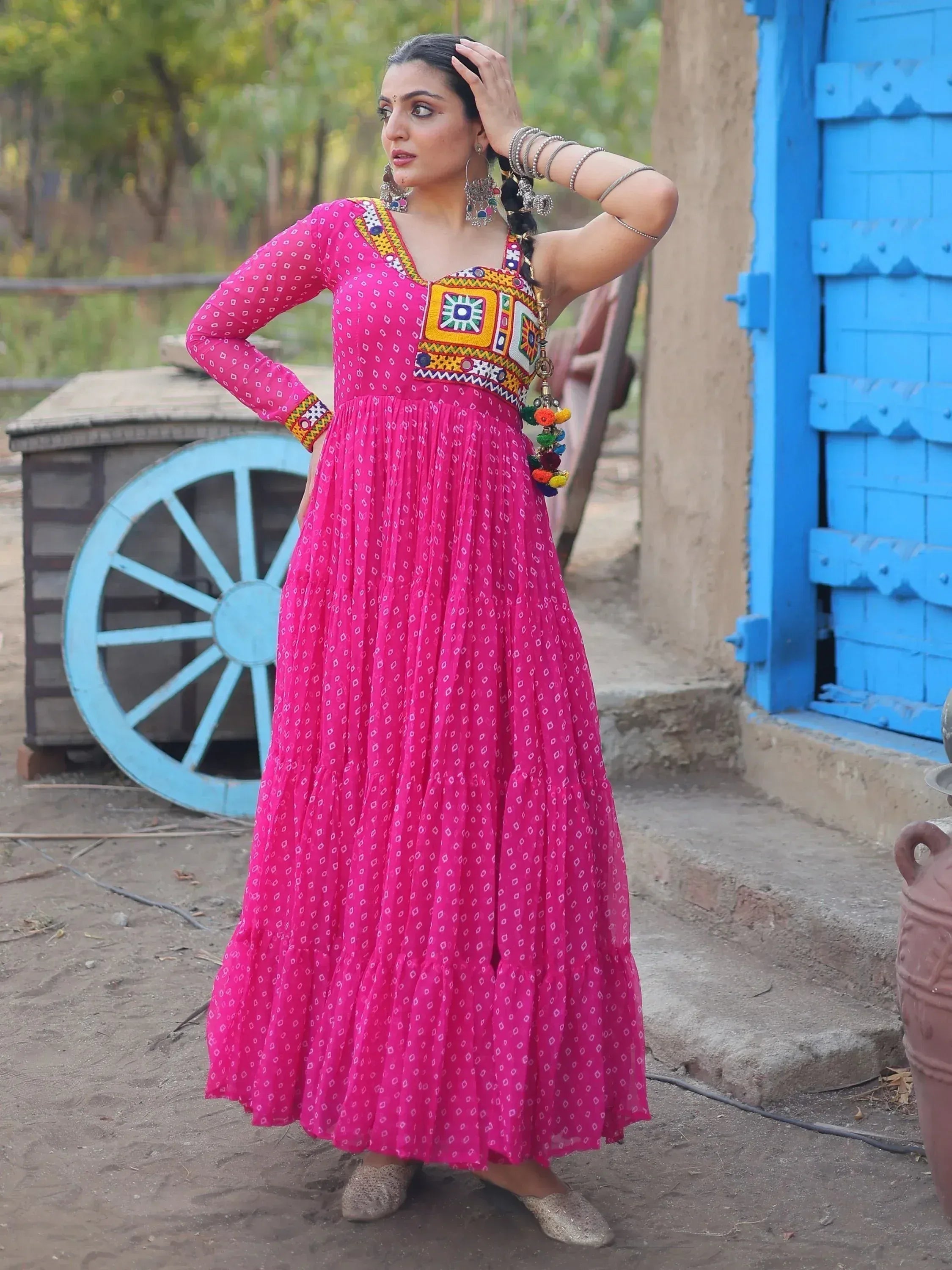 Pink ethnic gown with mirror work and pom poms, styled with jhumkas and bangles for festive occasions